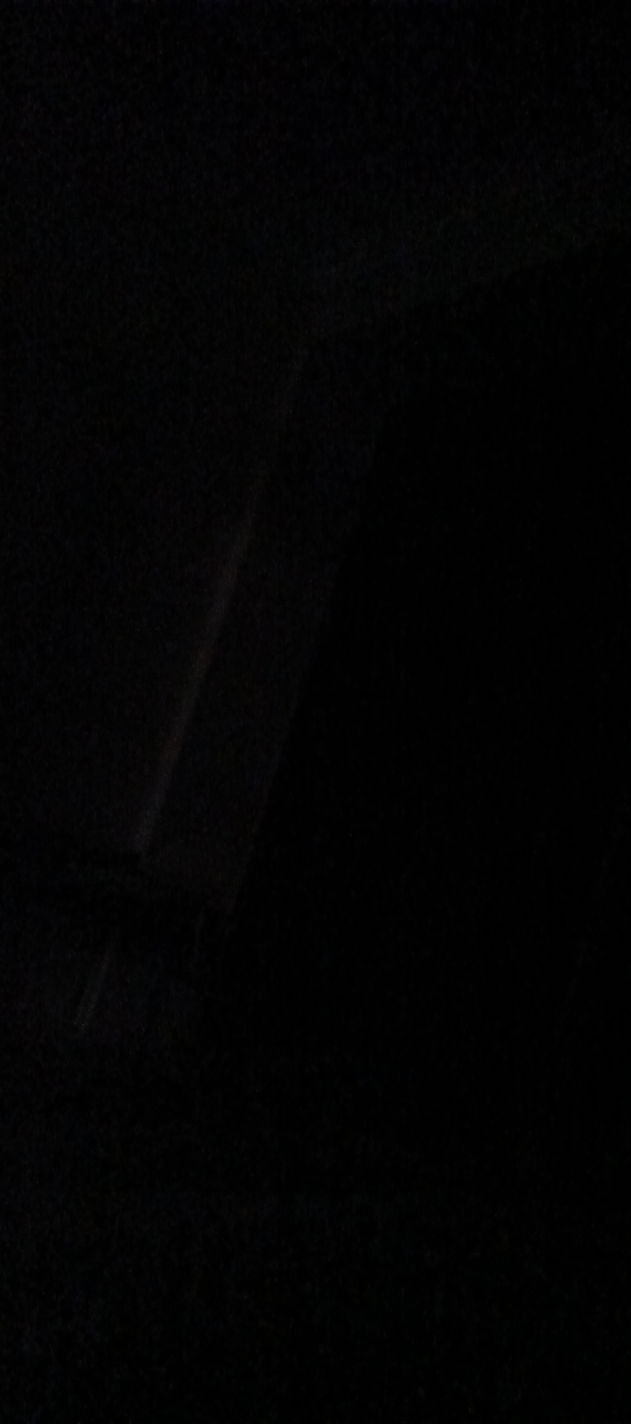 The image is dark and appears to be taken at night or in a dimly lit environment. There are faint streaks of light visible, suggesting a light source, possibly artificial, that is either moving or partially obscured. The overall impression is one of obscurity and low visibility. Without further context or clearer details within the image, it is impossible to determine the location in the city of Khasavyurt, Russia, or provide any specific details about people, subjects, objects, actions, interactions, or the environment.