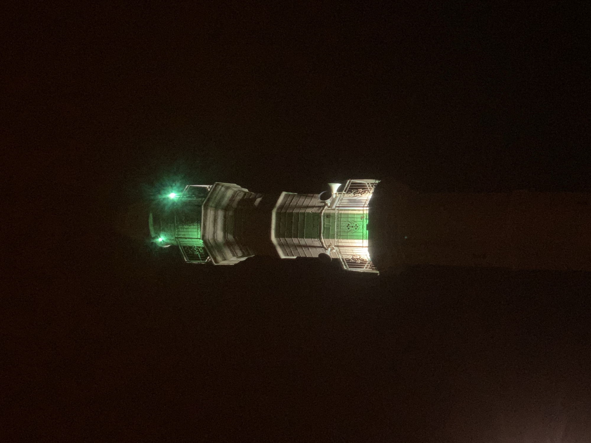 At night, an aerial view showcases the illuminated train structures located at the Tel Aviv Central railway station in Israel. The two trains are lit by green spotlights. The environment is predominantly dark, with the trains illuminated against the black background.