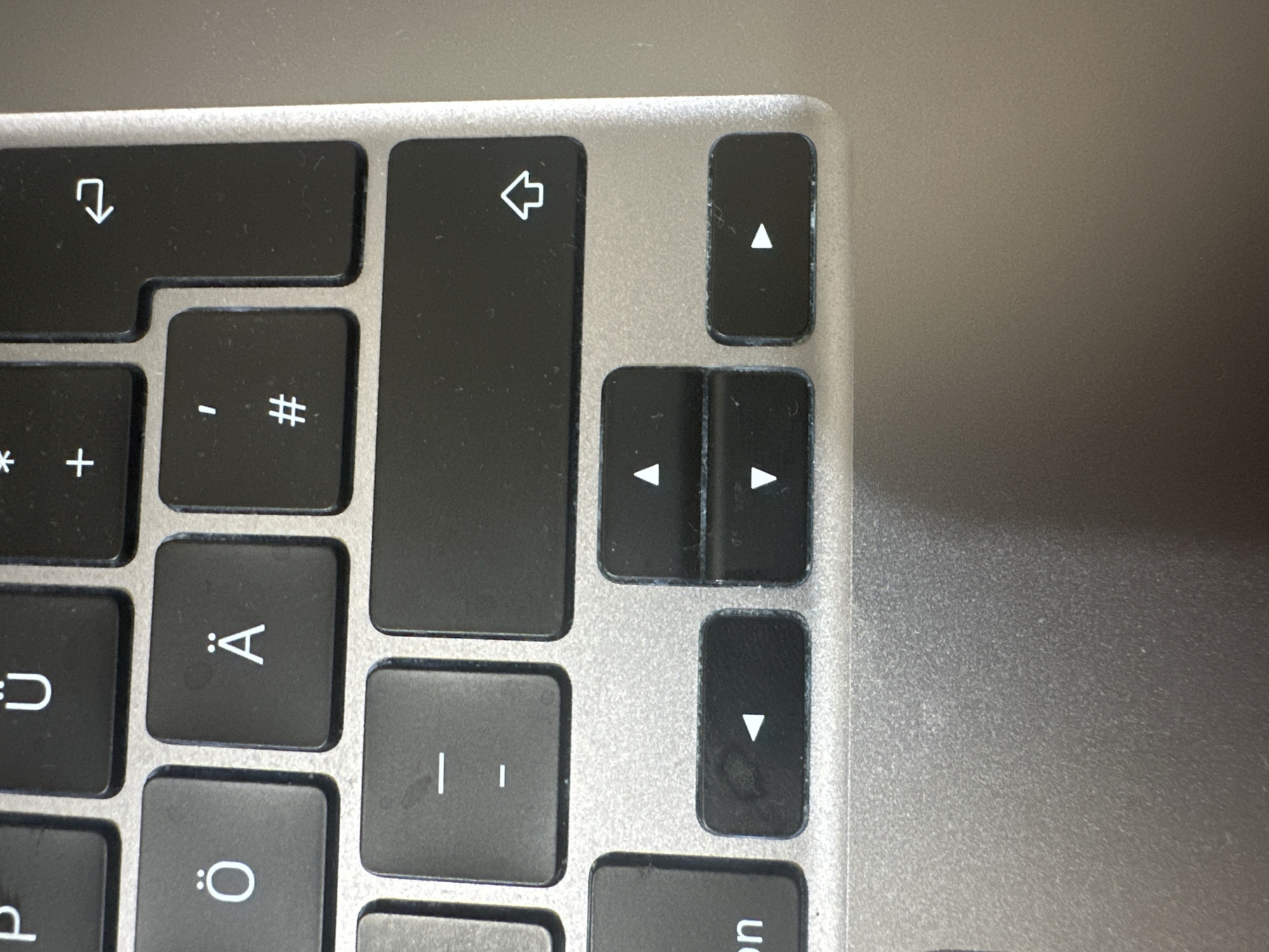 The image shows a close-up of a laptop keyboard. The keys are black with white characters. Visible keys include "P", "Ü", "+", an arrow pointing right, "Ö", "Ä", "'", "#", a horizontal line, two horizontal lines, an arrow pointing up, an arrow pointing left, an arrow pointing down, and an arrow pointing right. The keyboard is silver. The scene appears to be indoors on a desk or table, with the laptop open. There are no people or animals visible in the image. The location is not specified and there is no information about Hamburg, Germany.