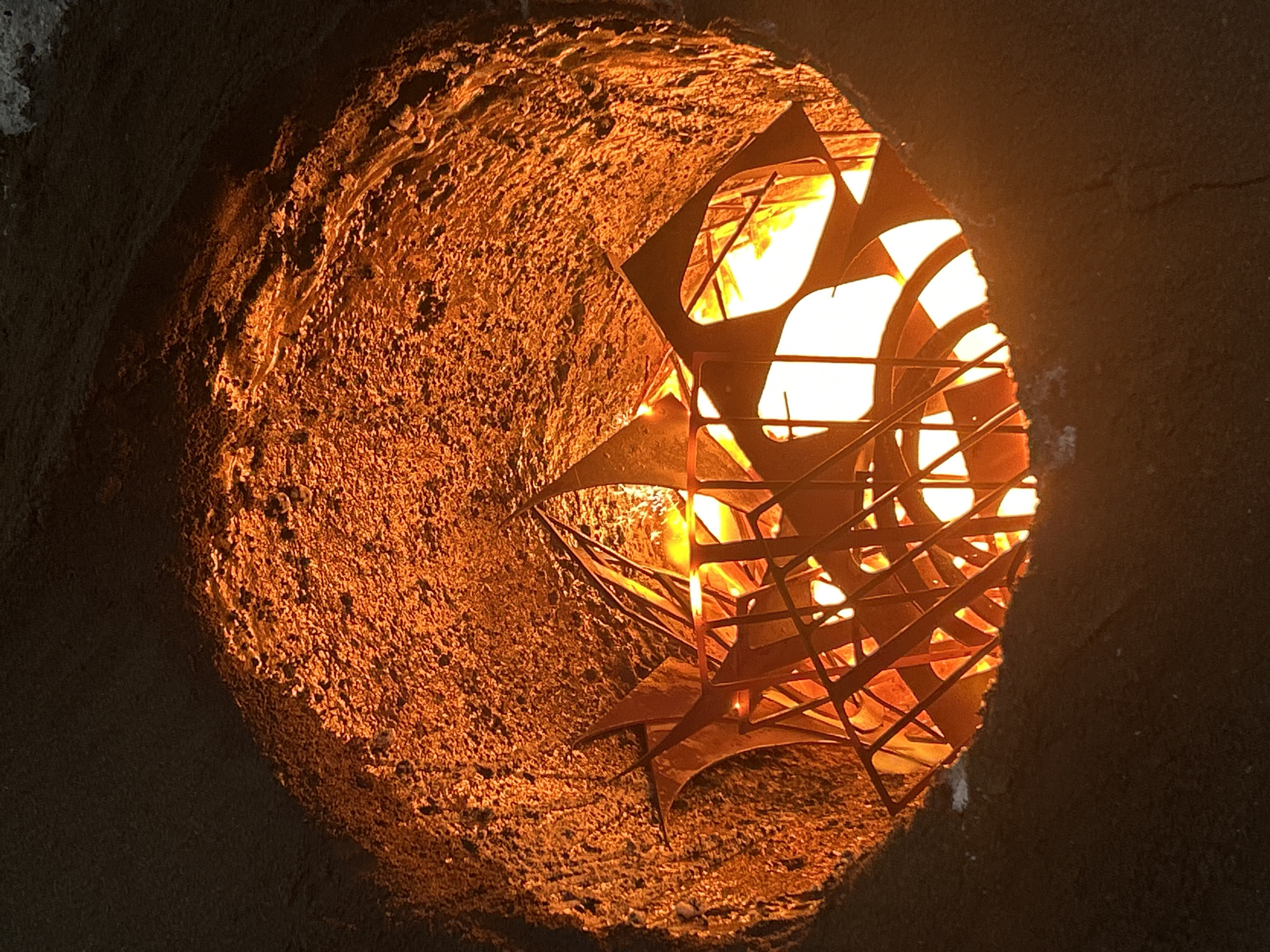 The image shows a cylindrical structure made of textured, possibly earthen material, with a circular opening revealing an internal structure made of intersecting metal shapes illuminated by a bright light source from within. The location is not identifiable as Noviy, Russia from the image alone.