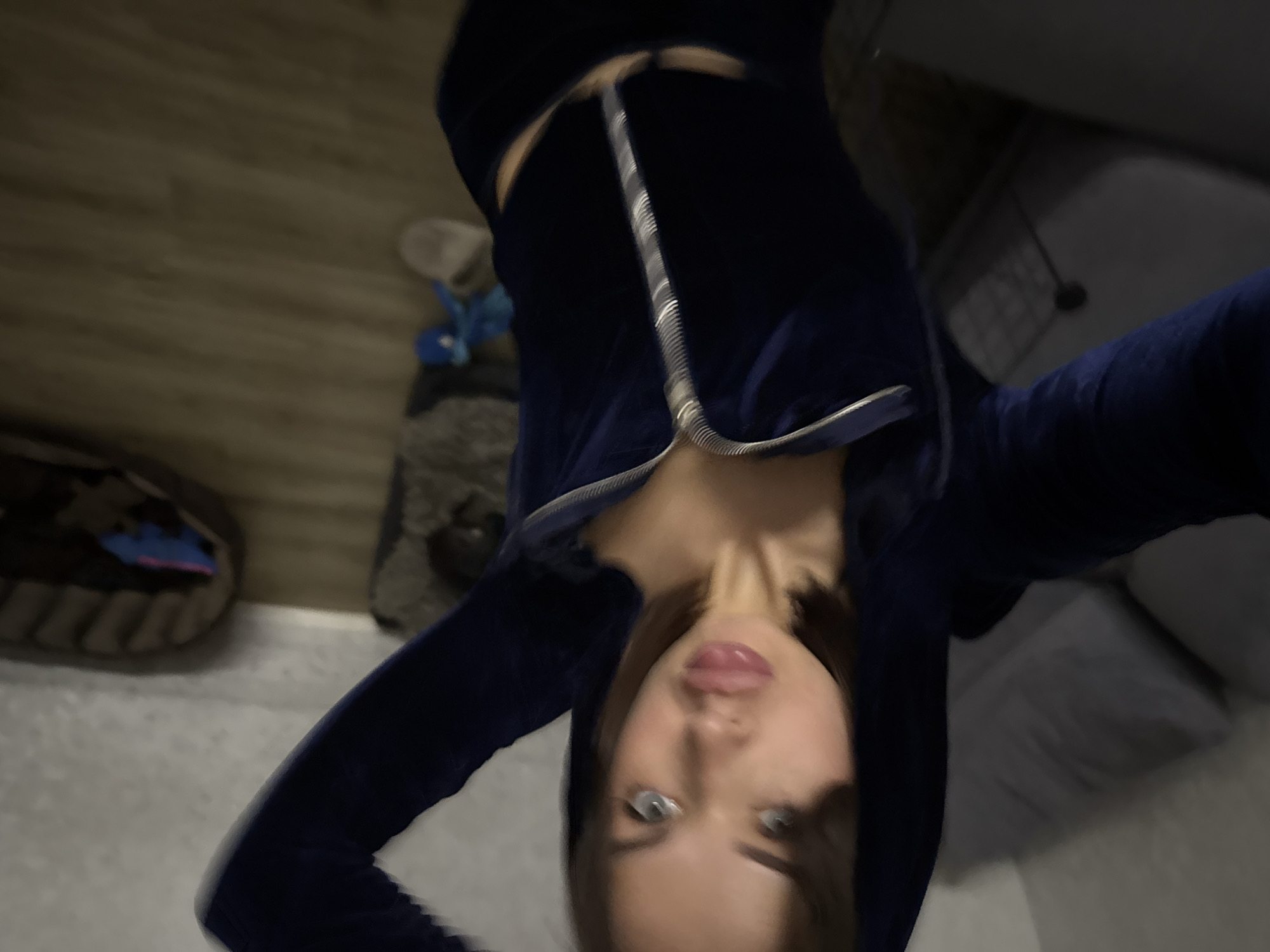A woman in a blue zip-up hoodie is shown from a top-down perspective. The background shows a wooden floor, a dog bed, and a portion of a gray couch. The location is Лобаново, Russia.