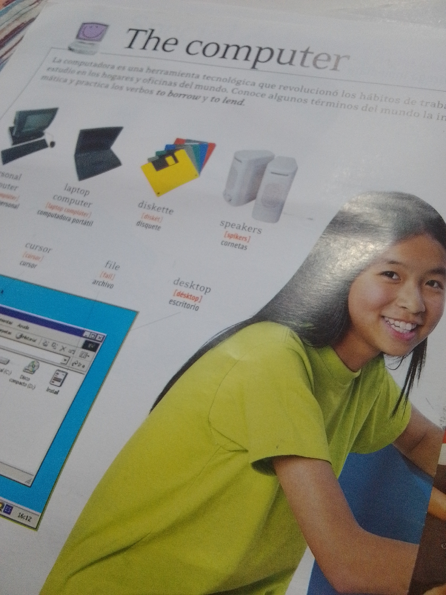 The image shows a close-up of a page from a book, with text and various computer-related images. The title "The computer" is prominently displayed. Below the title, there is a paragraph of text in Spanish, discussing computers as technological tools that have revolutionized habits. To the left, there are illustrations of a desktop computer, a laptop, and floppy disks. Further down, there are labels for "cursor" and "file" with their Spanish translations. On the right side, there are images of speakers with the label "speakers" and its Spanish translation. A portion of a computer screen with a file explorer interface is visible in the bottom left corner, displaying options like "Disco (C)" and "Instal." The main subject of the image is the content of the book page, with no indication of location in La Tagua, Venezuela or any other geographical context. There is no discernible action or interaction between people, as the only human element is a partial view of a smiling young girl with dark hair, wearing a bright yellow t-shirt, whose arm and shoulder are visible on the right side of the frame. The background is plain white, suggesting it is a page from a printed publication.