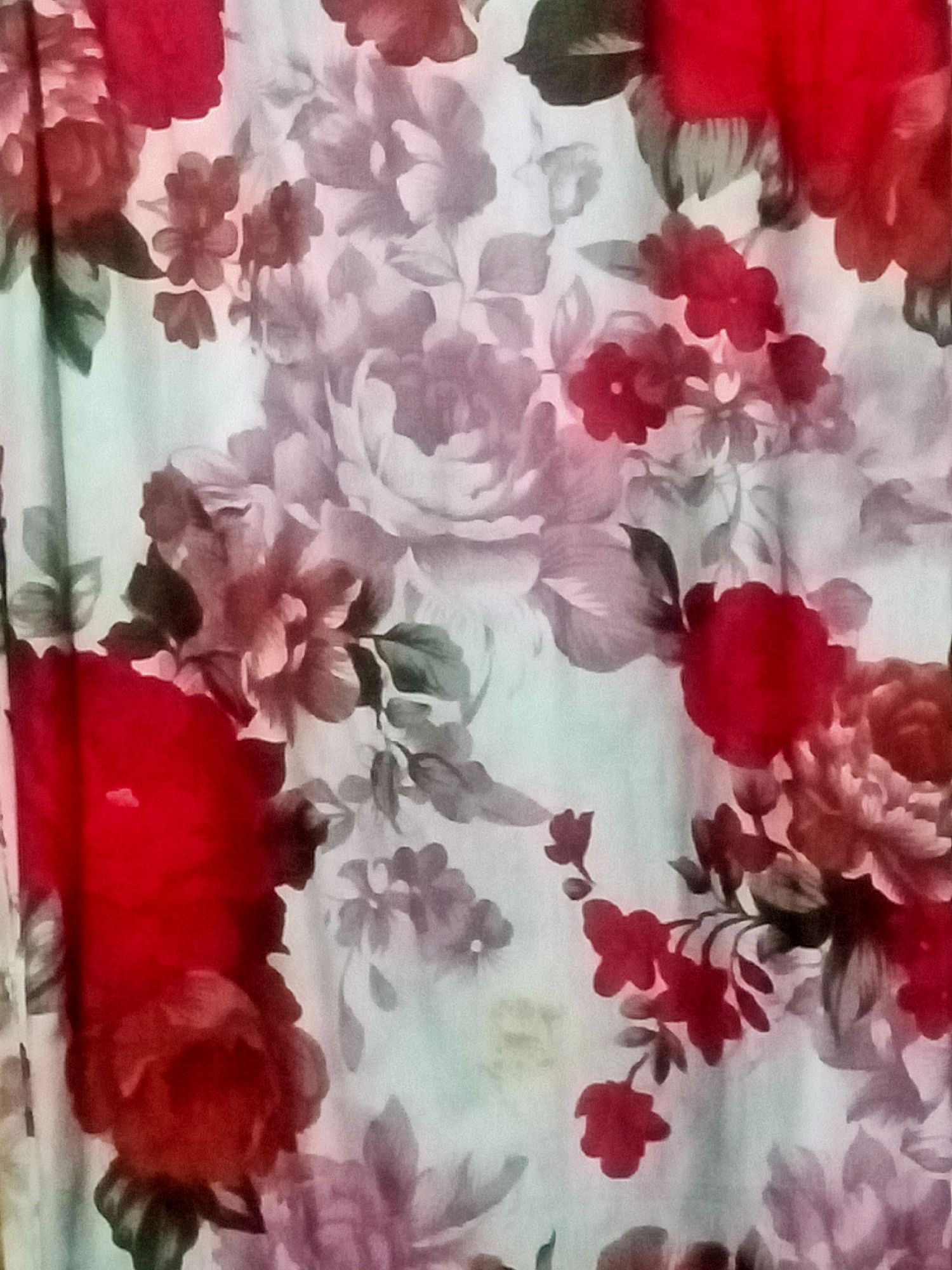 The image displays a close-up view of a fabric with a floral pattern. The pattern consists of various flowers and leaves rendered in shades of red, pink, and grey against a light, muted background. The flowers are depicted in a painterly style, with soft edges and blended colors. Some of the larger flowers are in full bloom, while others appear as buds or are partially obscured. The overall impression is of a vintage or romantic textile design. There is no discernible location in Nusa Agung, Indonesia, within this image.