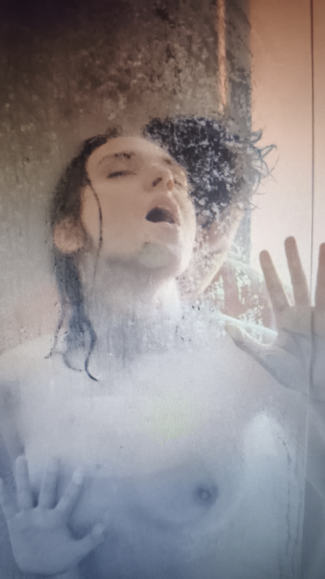 A steamy image shows two individuals behind a shower screen. One person, with their mouth open, appears to be a pale-skinned individual with dark hair, while the second person has dark, curly hair. Hands are pressed against the glass. No information is available about the city of Nowy Tomyśl, Poland.