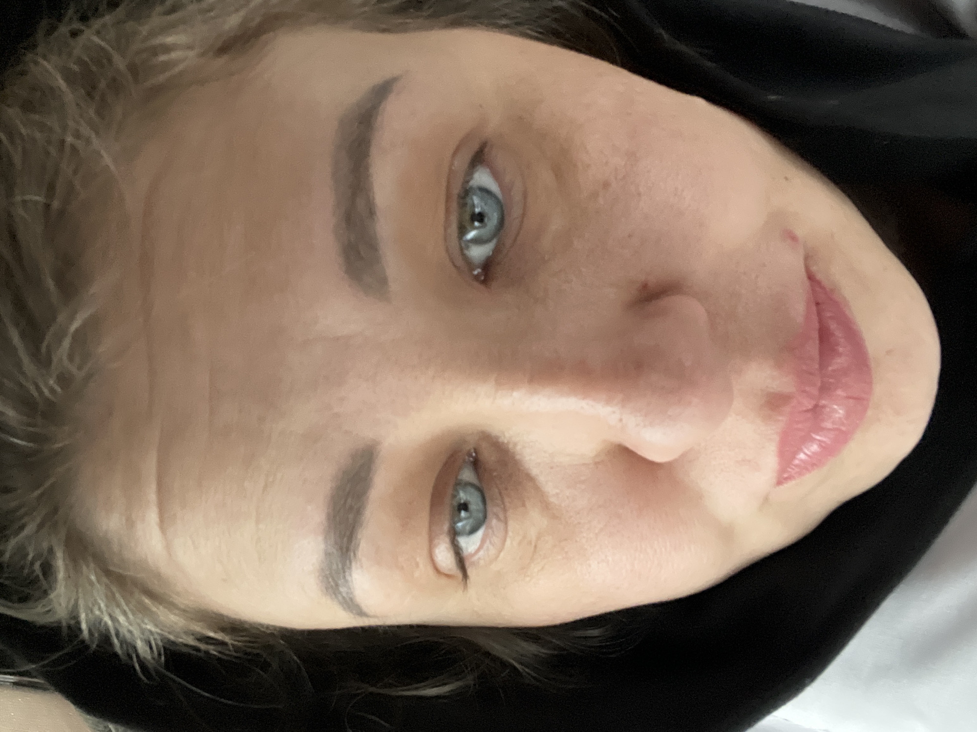 A close-up, slightly rotated image features a light-skinned person with blue eyes, light brown eyebrows, and pink lips. The person is wearing what appears to be a dark or black hood or garment. The background is indistinct, suggesting an indoor setting. There's no indication of location in Chaikovsky, Russia, or any specific city or environment. The focus is entirely on the person's facial features.
