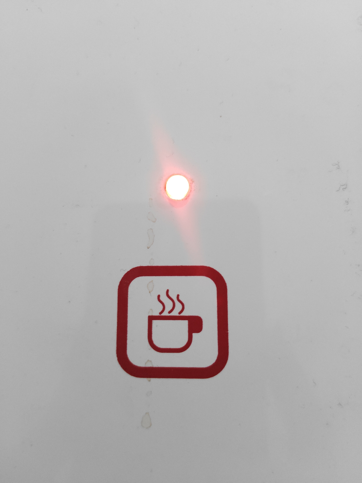 The image shows a close-up view of a white surface with a red icon of a steaming cup. A small, round red light is illuminated above and slightly to the left of the icon. The surface has some smudges and marks. The context of Semambung, Indonesia is not visually present in the image.