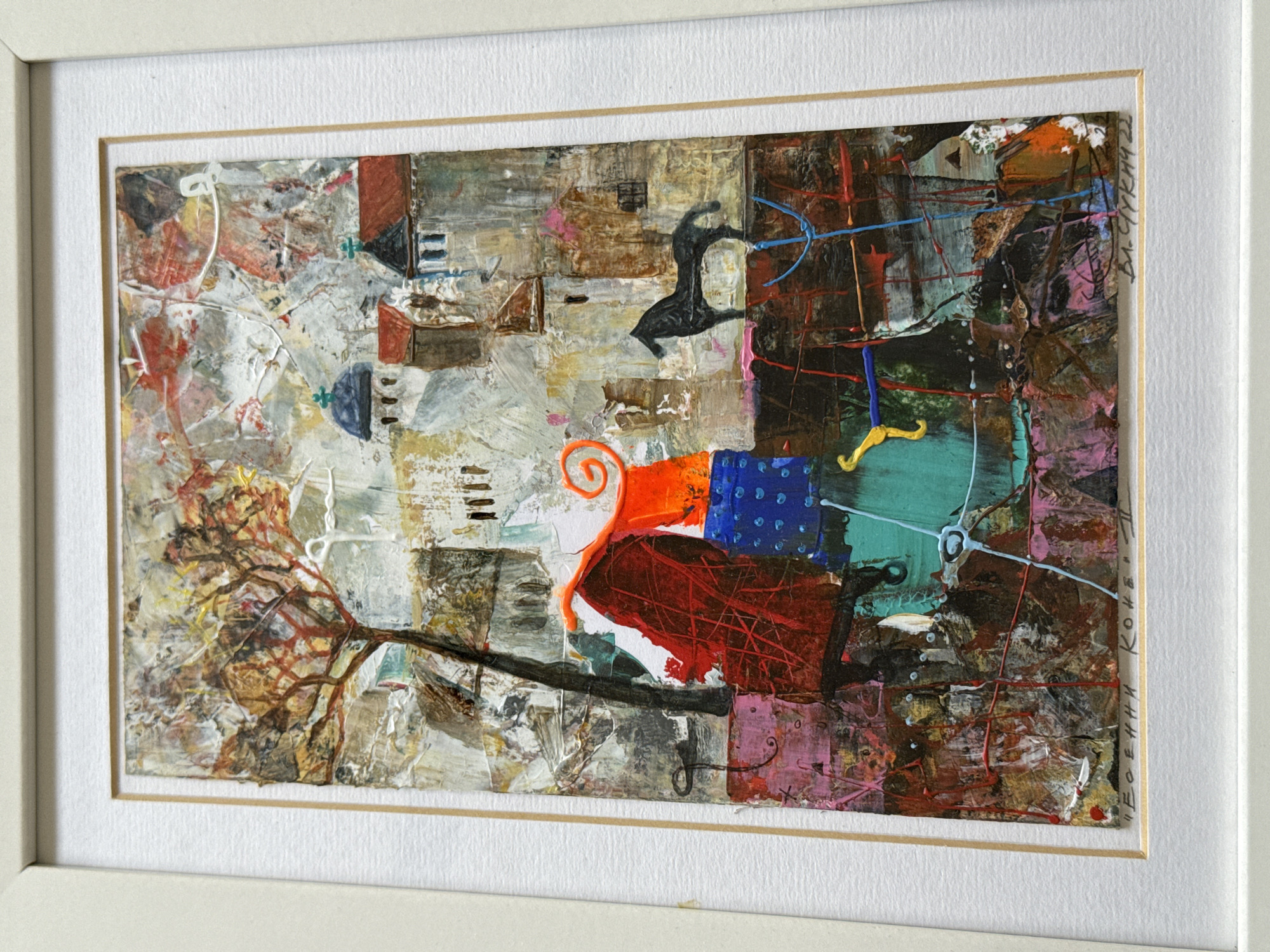 The image shows a framed abstract painting. The painting is predominantly brown, white, red, blue, and turquoise. It features a leafless tree branch extending horizontally across the lower portion, from the left. Above the branch, there are abstract shapes and colors, including a red area with a swirl of orange on top of a blue patch. There is a black silhouette of a figure on the right-hand side. The painting is signed on the lower right corner with a name ending in "KOHR" and the date "22." The painting is framed with a double border: a thin gold one directly around the painting, with a wider white border surrounding that. Based on the signature, the painting is by an artist named Evgeni Kohn. The painting is not located in Sofia, Bulgaria, it is a painting.