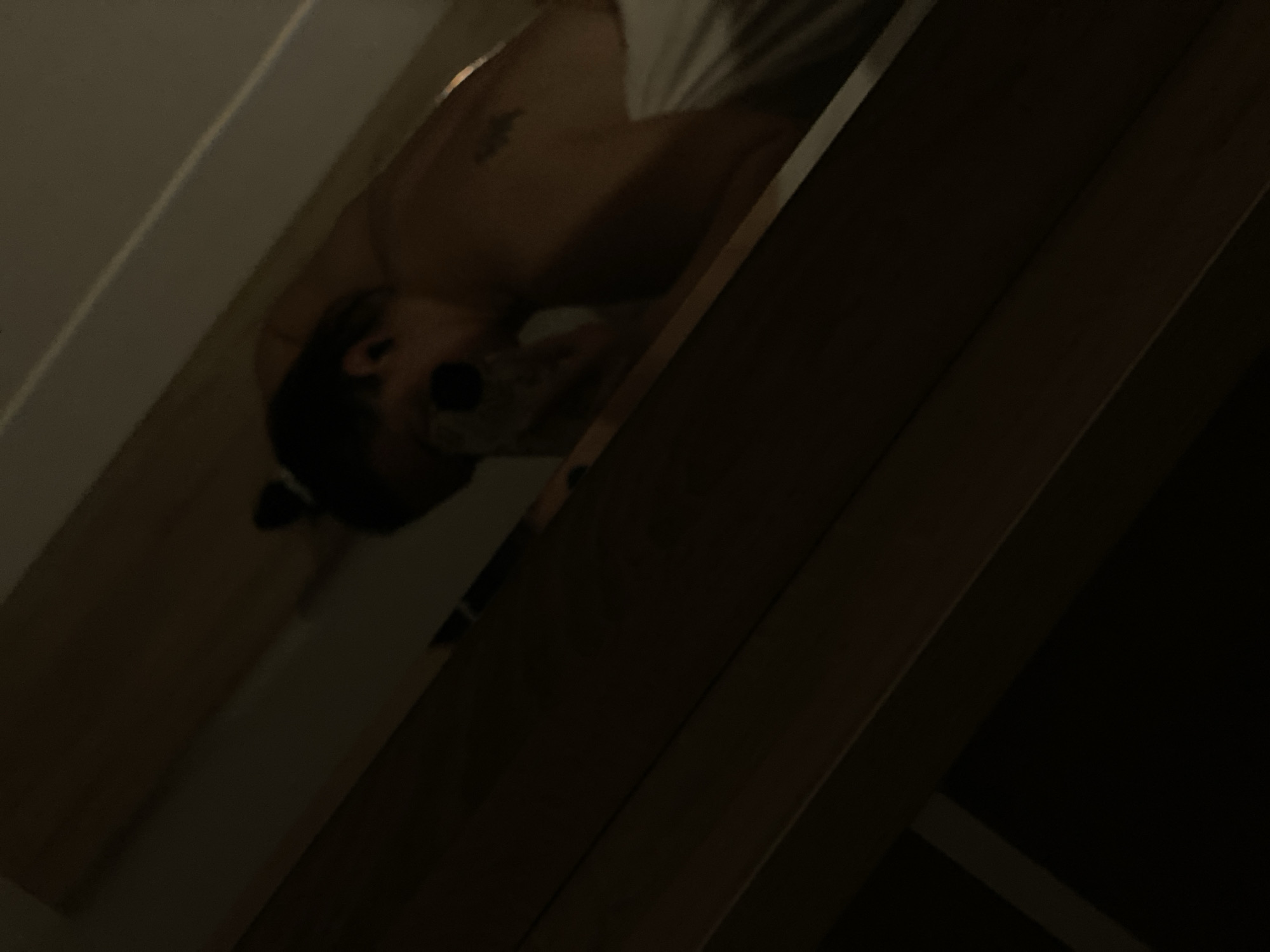The image, taken at an angle, depicts a partially visible individual in what appears to be an indoor environment. The person has dark hair and a visible tattoo on their torso. They are wearing a white garment. The background is comprised of wooden structures and a white wall. Specific location details within Sochi, Russia, are not discernible from the provided image.