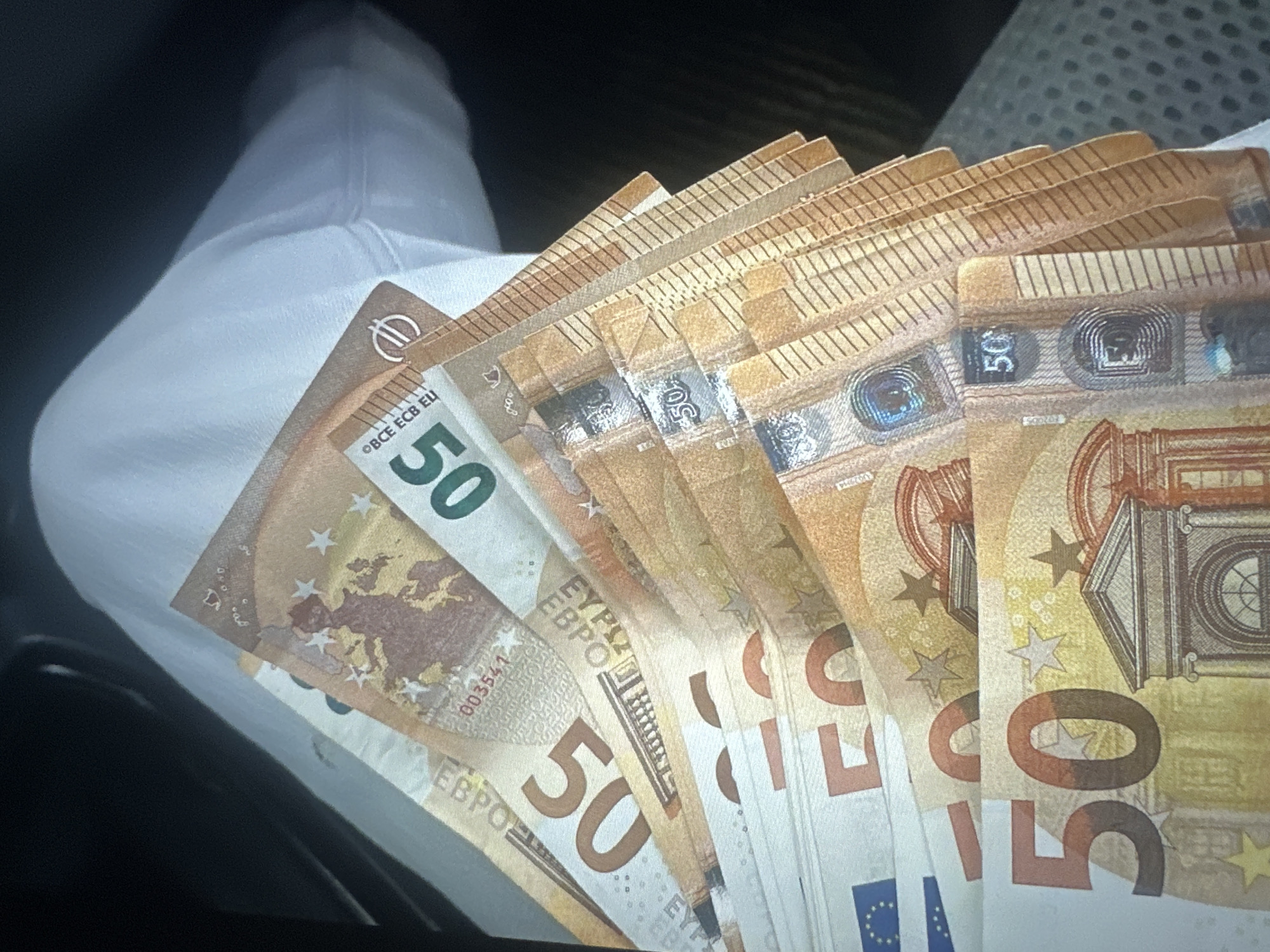 A fan of 50 euro banknotes is splayed out on a light-colored, textured surface, possibly fabric. The banknotes display prominent "50" markings and architectural imagery characteristic of European currency. The lighting suggests an indoor setting, and the composition is close-up, focusing entirely on the money. There is no indication of the location in Tallinn, Estonia.