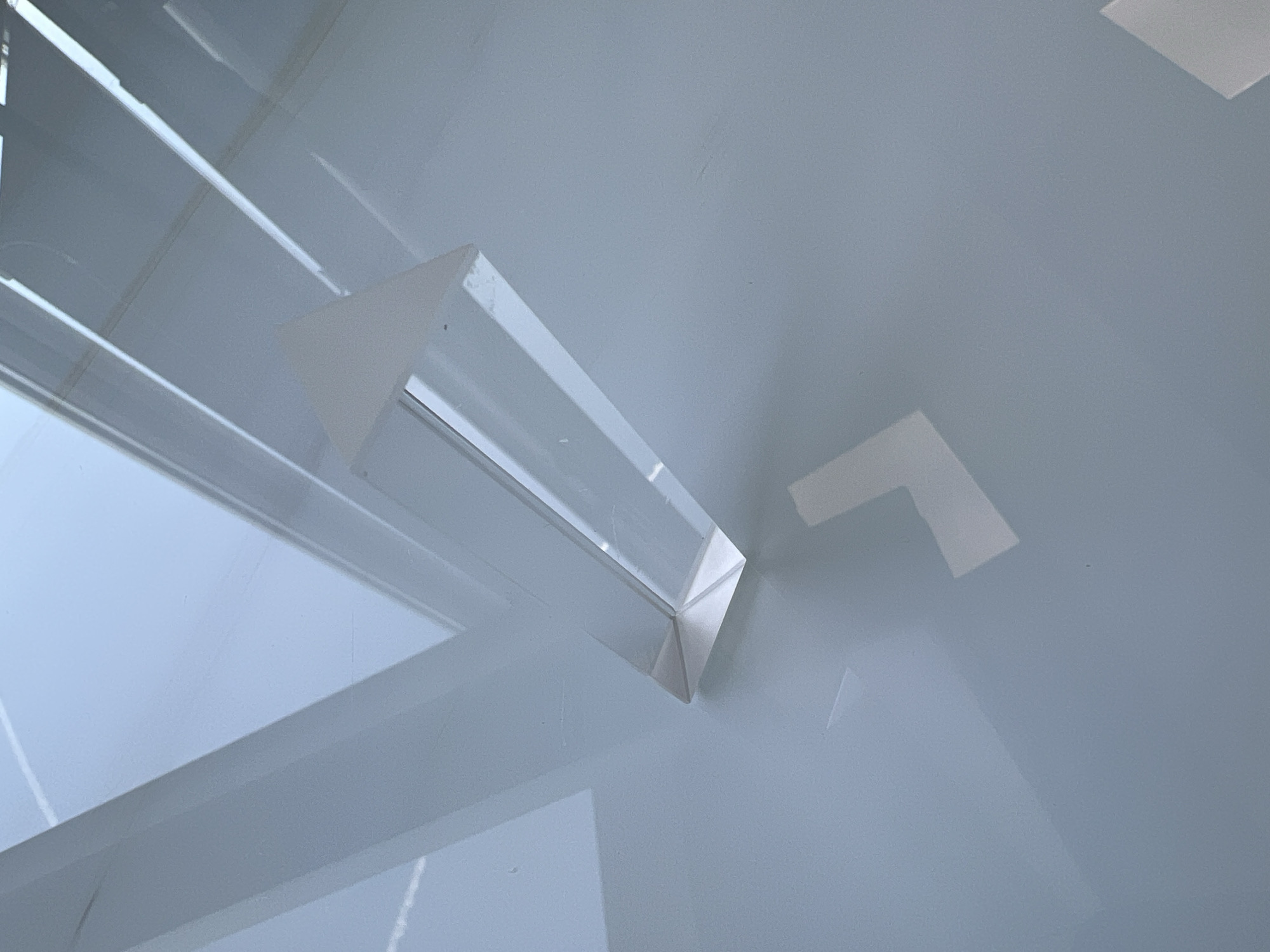 The image shows a triangular prism refracting light onto a white surface. The prism is made of a clear material, possibly glass or acrylic. Light from a window or other source is passing through the prism, creating a refraction pattern on the surface. The surface appears to be a table or other flat, white surface. The image provides insufficient information to determine a location in Moscow, Russia.