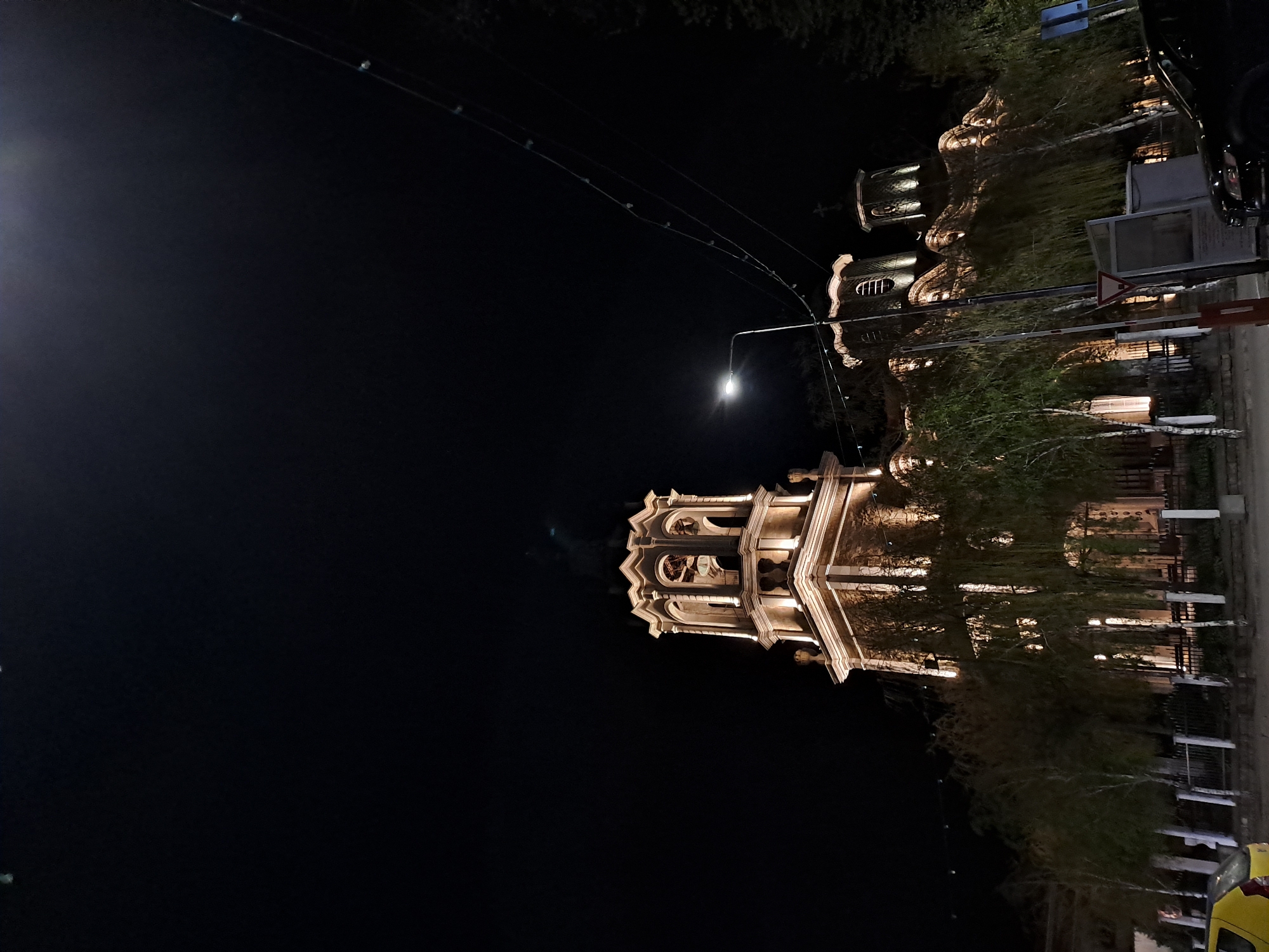 At night, a building is illuminated. It is located in an unknown city. The sky is dark. A streetlamp is visible.