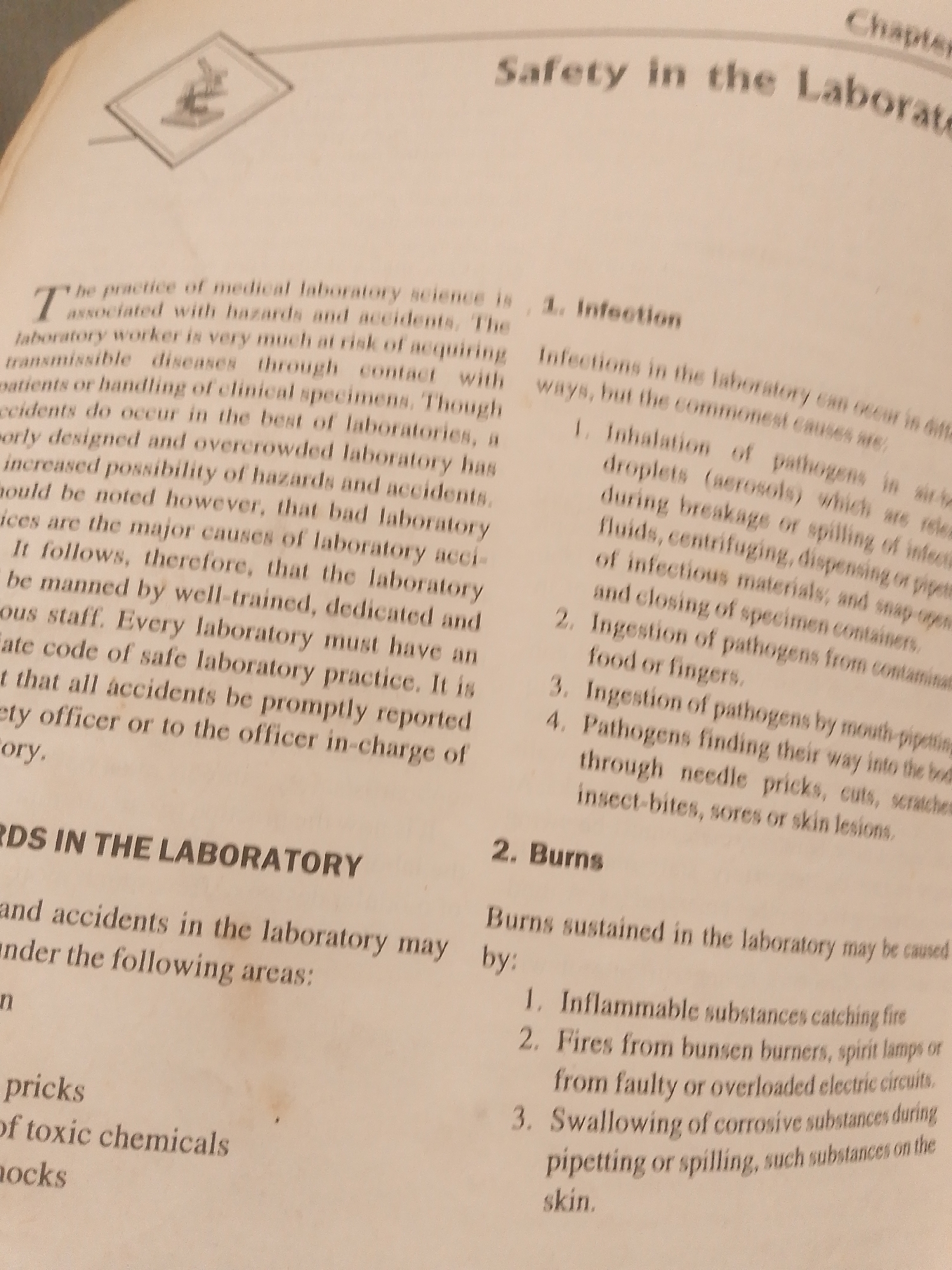 The image shows a page from a book or document with text and a small illustration. The text discusses safety in the laboratory, specifically covering "Infection" and "Burns." The illustration at the top left depicts a microscope within a framed square. The content is written in English and is presented in a formal, instructional tone. There is no visible information within the image that relates to the city of Jalingo, Nigeria, or any specific geographical location. The scene is limited to the printed page.