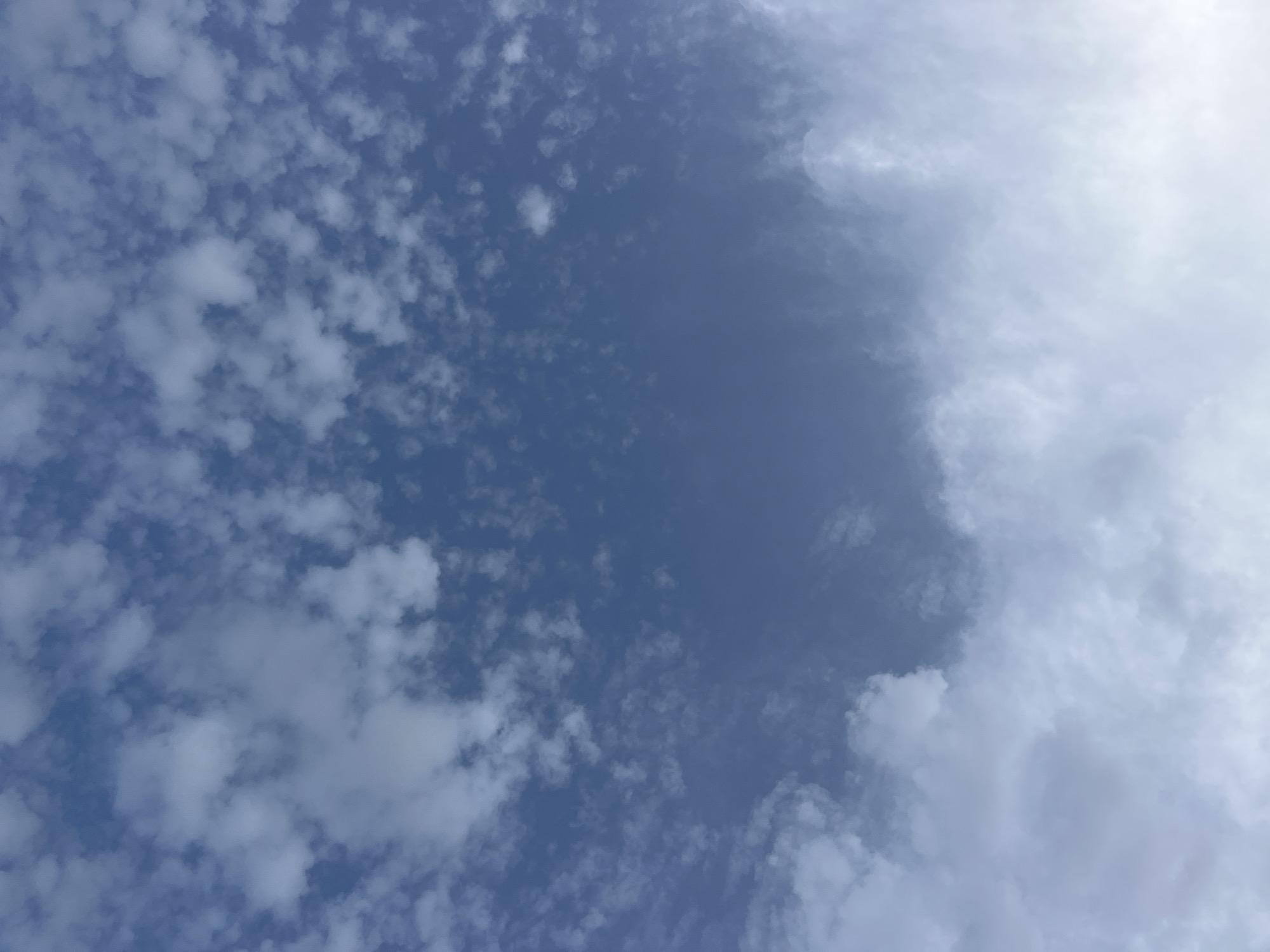 The image shows a wide expanse of blue sky filled with scattered white clouds. The clouds are varied in size and density, with some appearing wispy and thin, while others are thicker and more defined. The lighting suggests it is daytime, possibly late afternoon or early morning given the soft illumination. There are no discernible landmarks, people, or objects in the image, just the sky and clouds. The scene is devoid of any specific location indicators that would suggest it is in Jos, Nigeria, or any other city. The image is a purely natural scene of the sky.