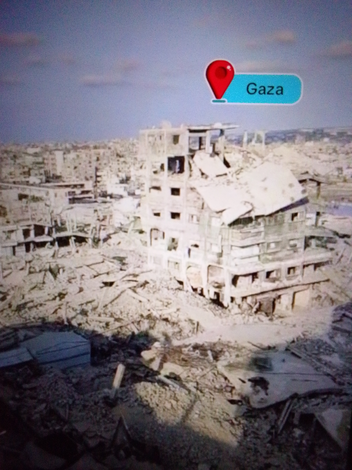 The image depicts a heavily damaged urban landscape with destroyed buildings and rubble. A marker with the text "Gaza" is visible in the upper right corner of the image, indicating the location. The destruction suggests a conflict or disaster has occurred. The environment is characterized by debris, collapsed structures, and an overcast sky. There are no visible people in the image. The image does not show the city of Aznakayevo, Russia.