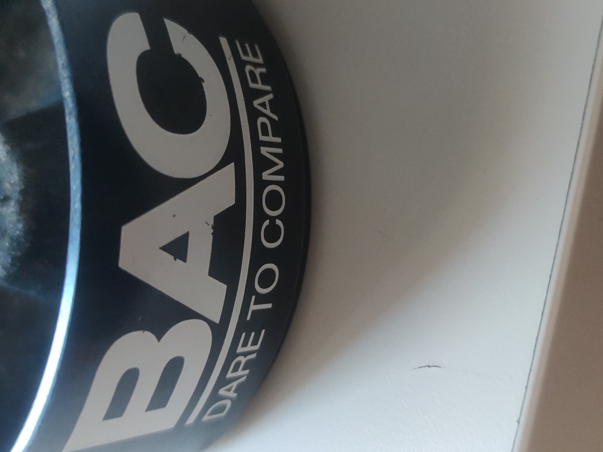 A black cylindrical object with white lettering reading "BAC" vertically and "DARE TO COMPARE" written along the circumference is on a white surface. The location is Unknown, Unknown.