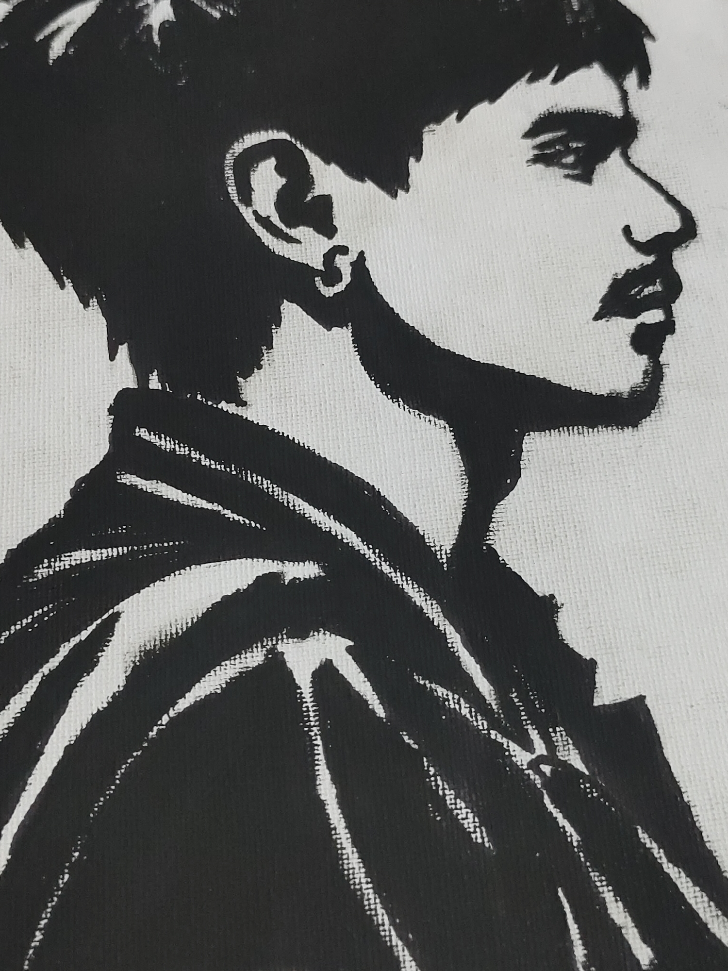 A high-contrast, black and white graphic portrait depicts an individual in right-facing profile. The subject appears male, with short, dark hair and a moustache. A small, circular hoop earring is visible in the left ear. The eye is open and directed slightly forward, above a prominent nose and defined lips. The upper torso is shown, with the subject wearing a dark garment, possibly a jacket or hooded top, rendered with angular white highlights that indicate folds and contours. The artwork utilizes stark black shapes against a textured white background, consistent with paint on canvas. No contextual environmental details are present to determine a specific geographical location, including within Davao City, Philippines.