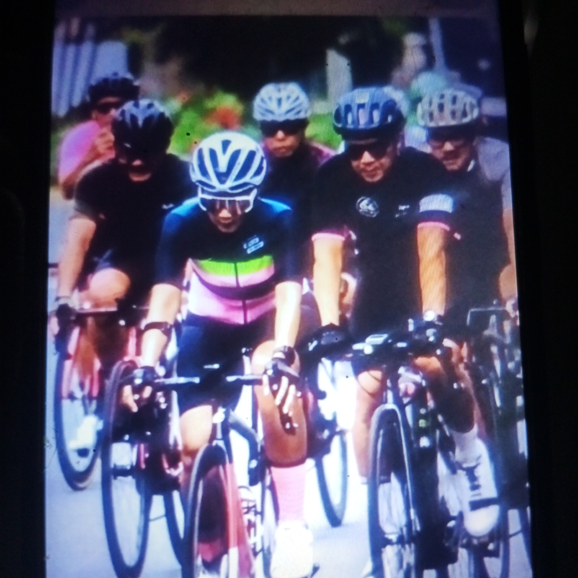 The image depicts a group of cyclists wearing helmets and cycling gear, participating in a race or group ride. They are positioned in a line, with some cyclists in the foreground and others in the background, suggesting a dynamic event. The cyclists are on road bicycles, and the environment appears to be an urban or suburban setting, possibly in Cemani, Indonesia, given the context. The lighting suggests it is daytime. The focus is on the cyclists and their activity, capturing the intensity of their participation.