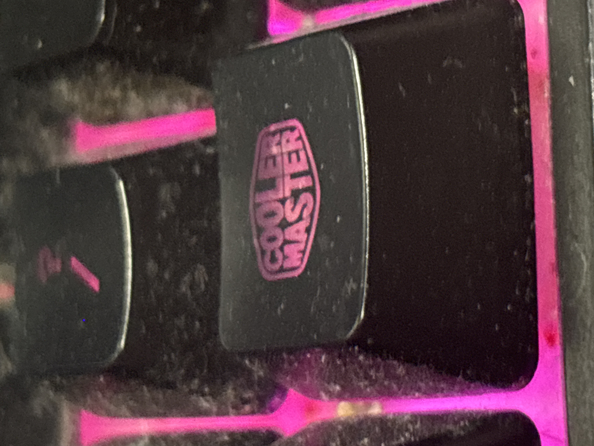 The image displays a close-up, angled view of a black keyboard key with the "Cooler Master" logo in pink. The key appears to be dirty with dust and smudges. Pink LED lighting is visible from beneath and around the keys, suggesting an illuminated gaming keyboard. The overall environment is dark and cluttered, indicating a personal computer setup. The image is a close-up and does not show any contextual information about Dimitrovgrad, Bulgaria.
