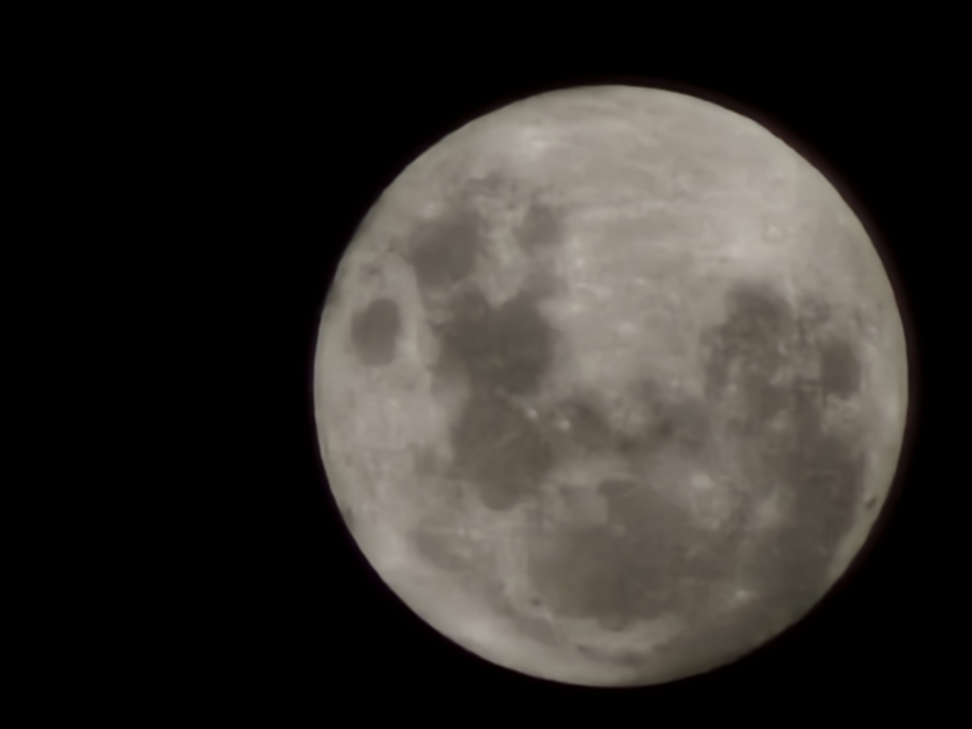 A full moon is prominently featured against a black background. The moon's surface shows varying shades of grey, with visible craters and textured patterns. The image is focused, and the details of the lunar surface are relatively clear. No other objects or features are visible besides the moon and the black background. The location in Esch-sur-Alzette, Luxembourg is not determined.