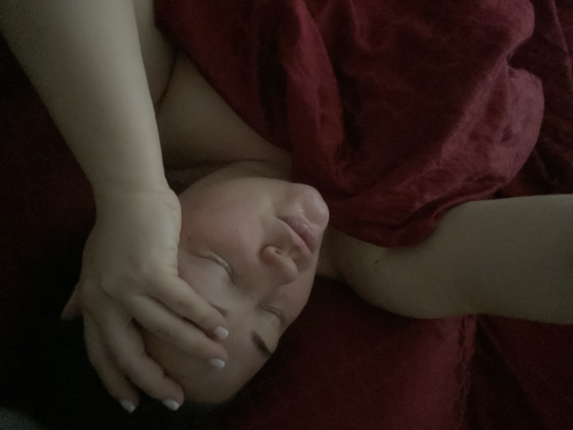 A person is lying down with their face obscured by their hand. The person is on a red surface, possibly a bed or blanket. The location is unknown and not identifiable from the image.