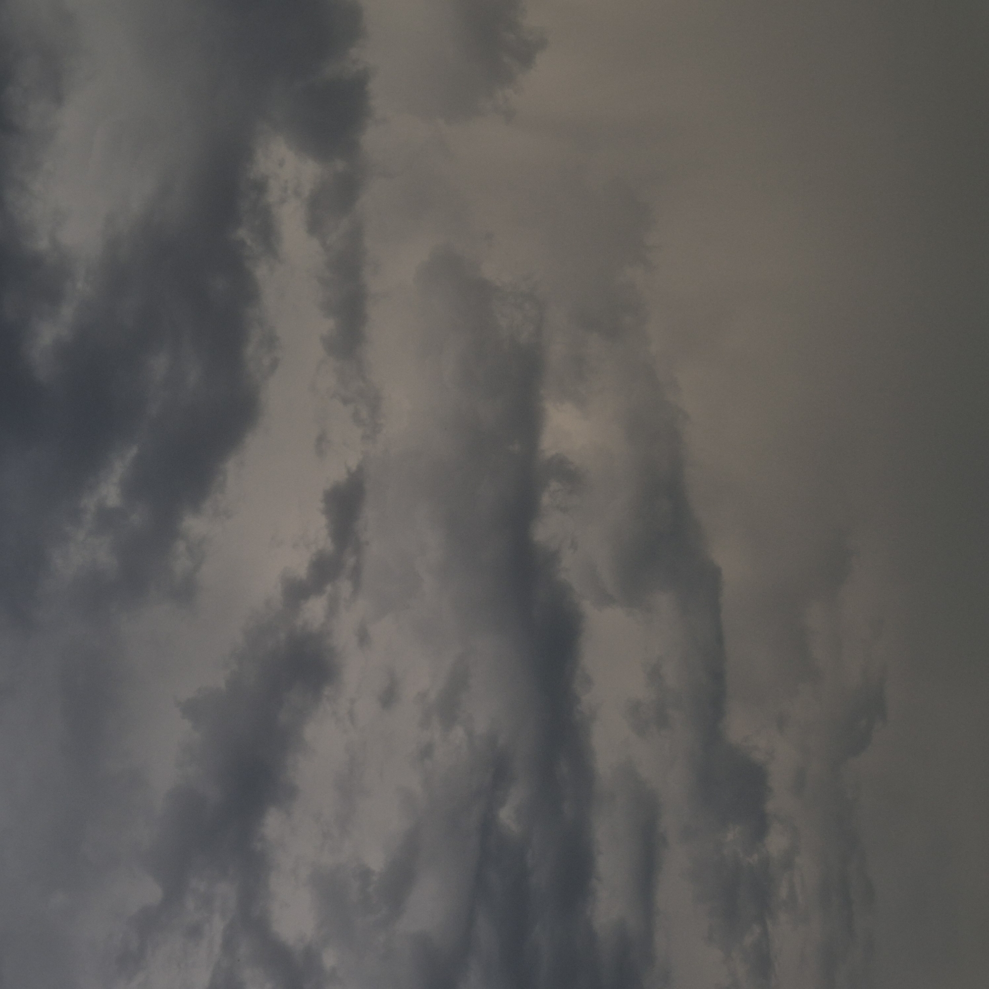 This is a medium shot of a cloudy sky. The clouds are dark and heavy, suggesting an overcast or stormy day. The overall color palette is muted, dominated by various shades of gray. There are no discernable landmarks or structures visible in the image, making it impossible to determine a specific location within Новостройка, Russia, or any other city. The image solely focuses on the atmospheric conditions of the sky.