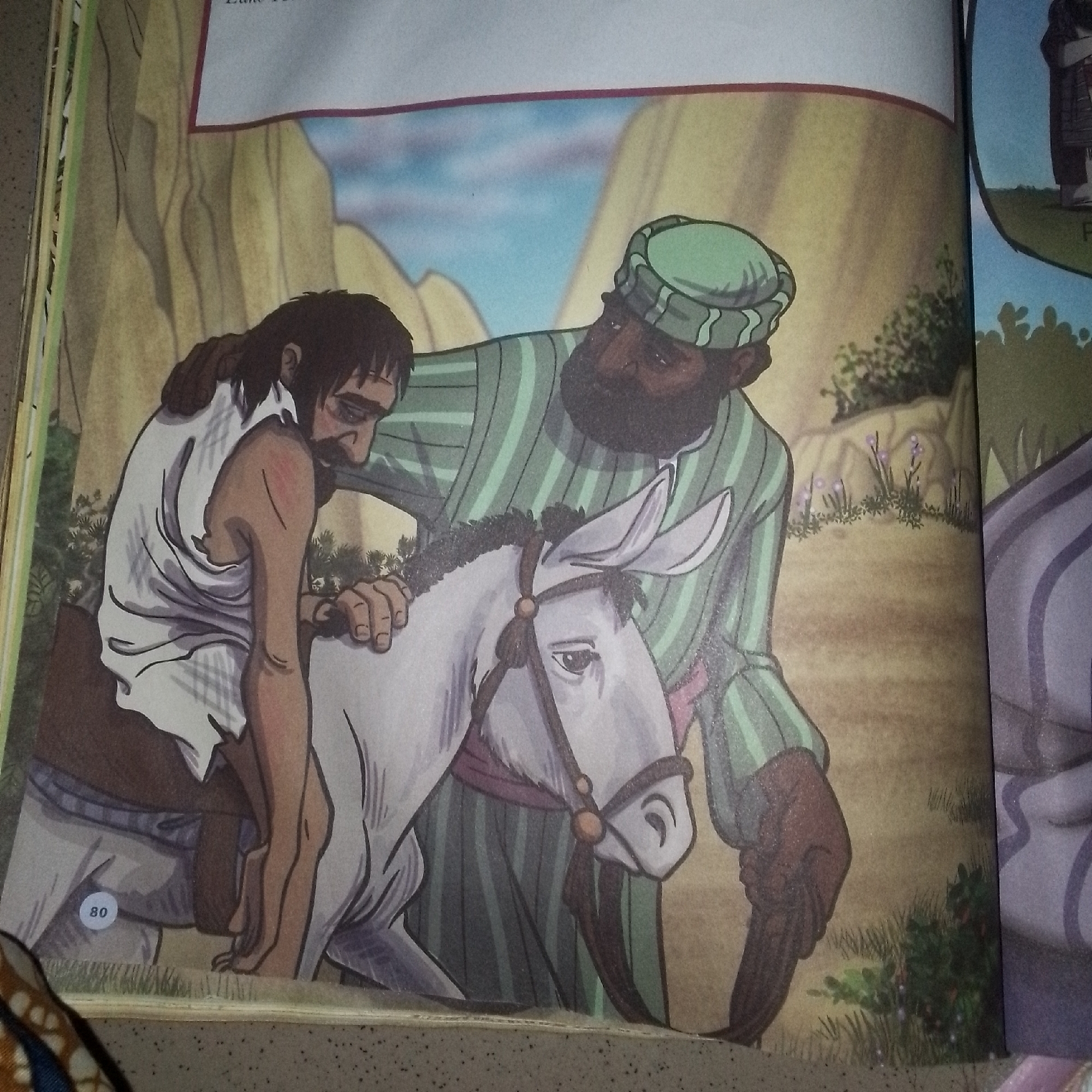 The image depicts two men and a donkey in a desert-like environment with rocky hills and sparse vegetation under a blue sky. On the left, a man with dark, unkempt hair and a beard, wearing a torn white garment, is slumped over the back of a white donkey. His arms are draped over the donkey's neck and hindquarters, suggesting exhaustion or injury. His face is turned down. To the right, a man with dark skin, wearing a green and white striped robe and a green turban, stands beside the donkey, placing a hand on the slumped man's back and another on the donkey's head. He appears to be supporting or aiding the injured man. The donkey has its ears perked and its eyes looking forward. A small circular badge with the number "80" is visible on the lower left side of the donkey's hindquarters. The environment is arid, with tan-colored earth and muted green foliage. In the background, a hazy mountain range suggests a remote or desolate location. The scene has a narrative quality, possibly illustrating a story of compassion or aid. There is no visible indication of the city of Jalingo, Nigeria, in this image.