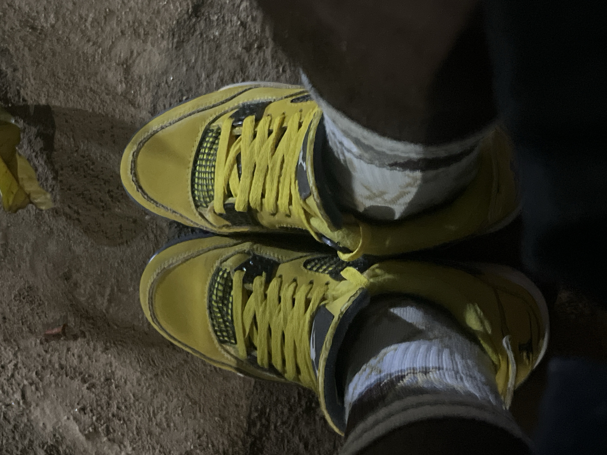A top-down shot depicts a pair of yellow sneakers worn on a person's feet, standing on a dirt or sand-covered surface. The sneakers are laced and have a textured pattern on the sides. White socks with stripes are visible between the shoes and the person's legs. The lighting suggests the photo was taken outdoors. There is no information that places this image in Jalingo, Nigeria.
