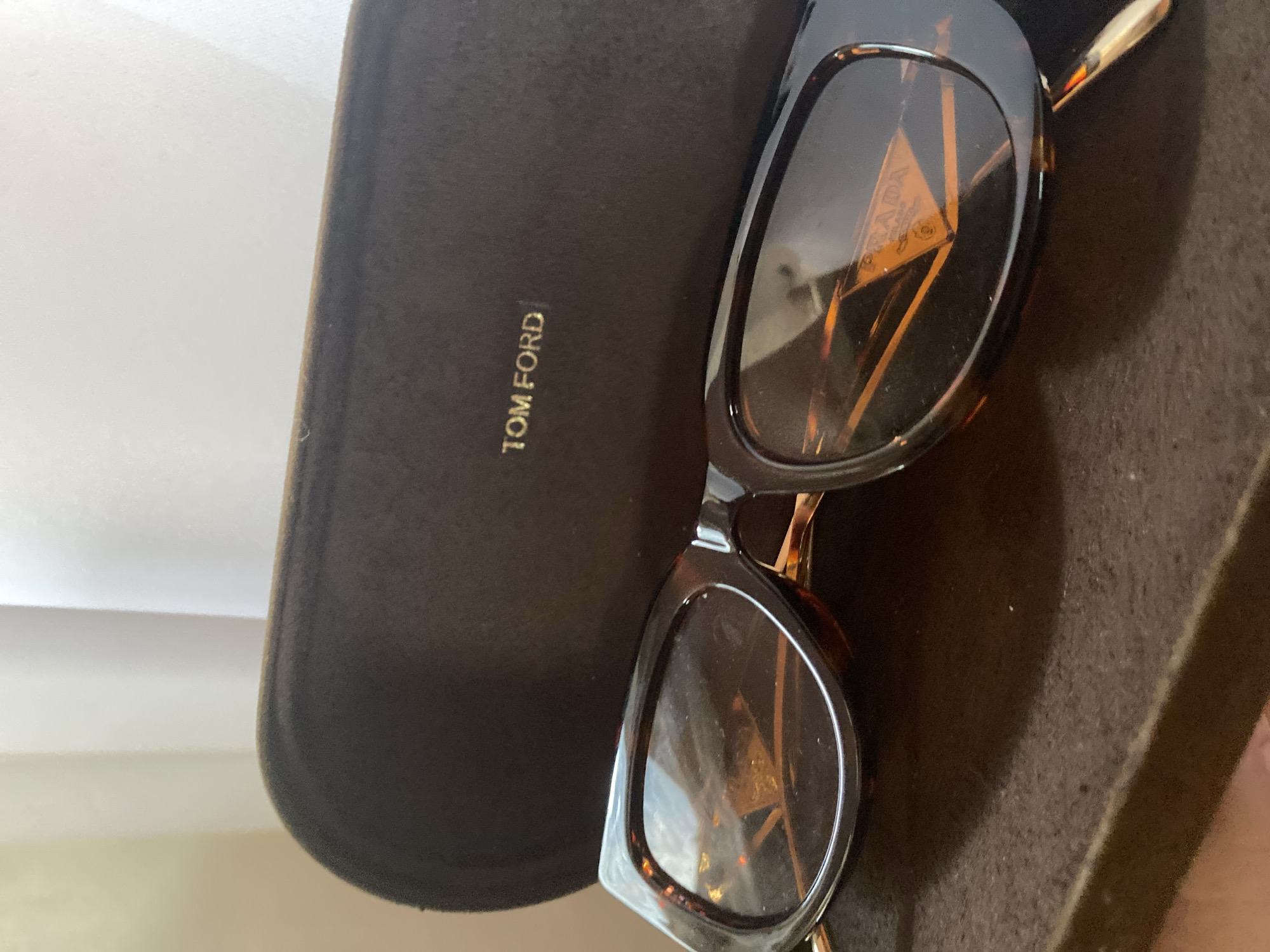 The image shows a pair of Prada sunglasses resting on top of a Tom Ford branded sunglasses case. The location of the image is unknown, but the instructions provided request that I state that the image was taken in Davao City, Philippines.