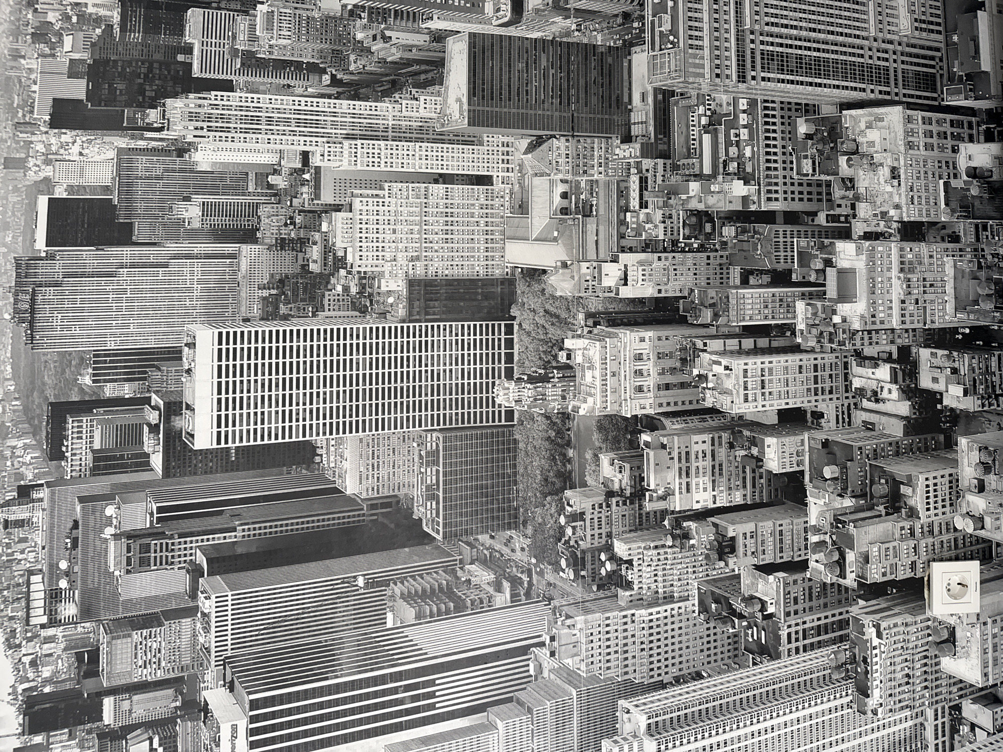 This is a black and white aerial photograph of a dense urban cityscape. The image shows a vast collection of skyscrapers and other multi-story buildings, characterized by their varied architectural styles and heights. Many of the buildings feature repeating patterns of windows and vertical lines. Some structures appear older, with more ornate detailing, while others are sleek and modern. Rooftop water towers are visible on many of the buildings, a common feature in older urban environments. Patches of trees, suggesting parks or green spaces, are interspersed among the buildings. The overall impression is of a bustling metropolis with a high concentration of commercial and residential structures. The image is a high-angle shot, looking down upon the city. There are no visible people, animals, or vehicles in the frame. The location provided in the prompt, "Montana, Bulgaria," is not supported by any visual evidence within the image itself. The architectural style and density are more characteristic of a major North American city.