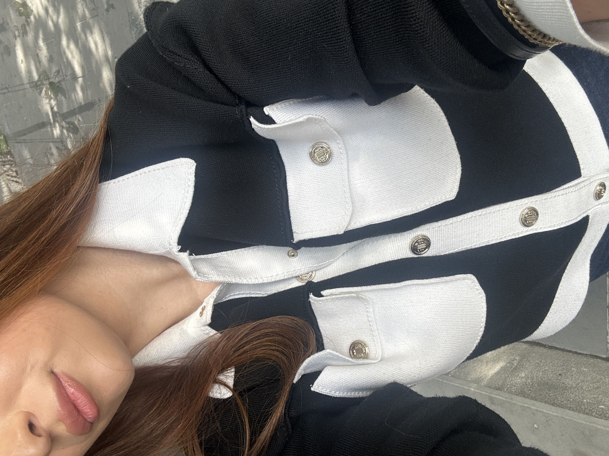 A person is wearing a black and white cardigan sweater with silver buttons. The location is not discernable from the image.