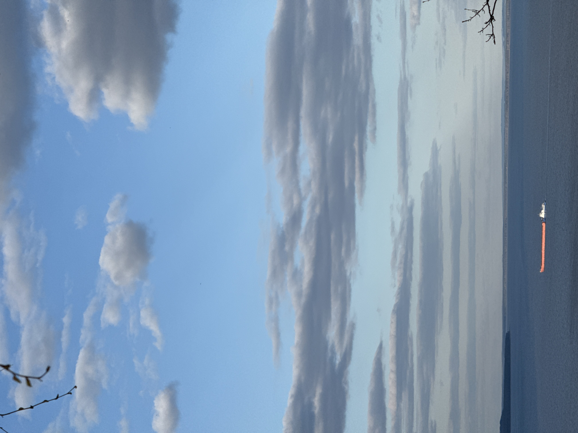 The image shows a body of water, possibly a large lake or sea, under a partly cloudy sky. The sky has a gradient of blue, with some white and gray clouds. The water is dark, reflecting the sky's color. A ship is visible on the water. The location is possibly Galevo, Russia.