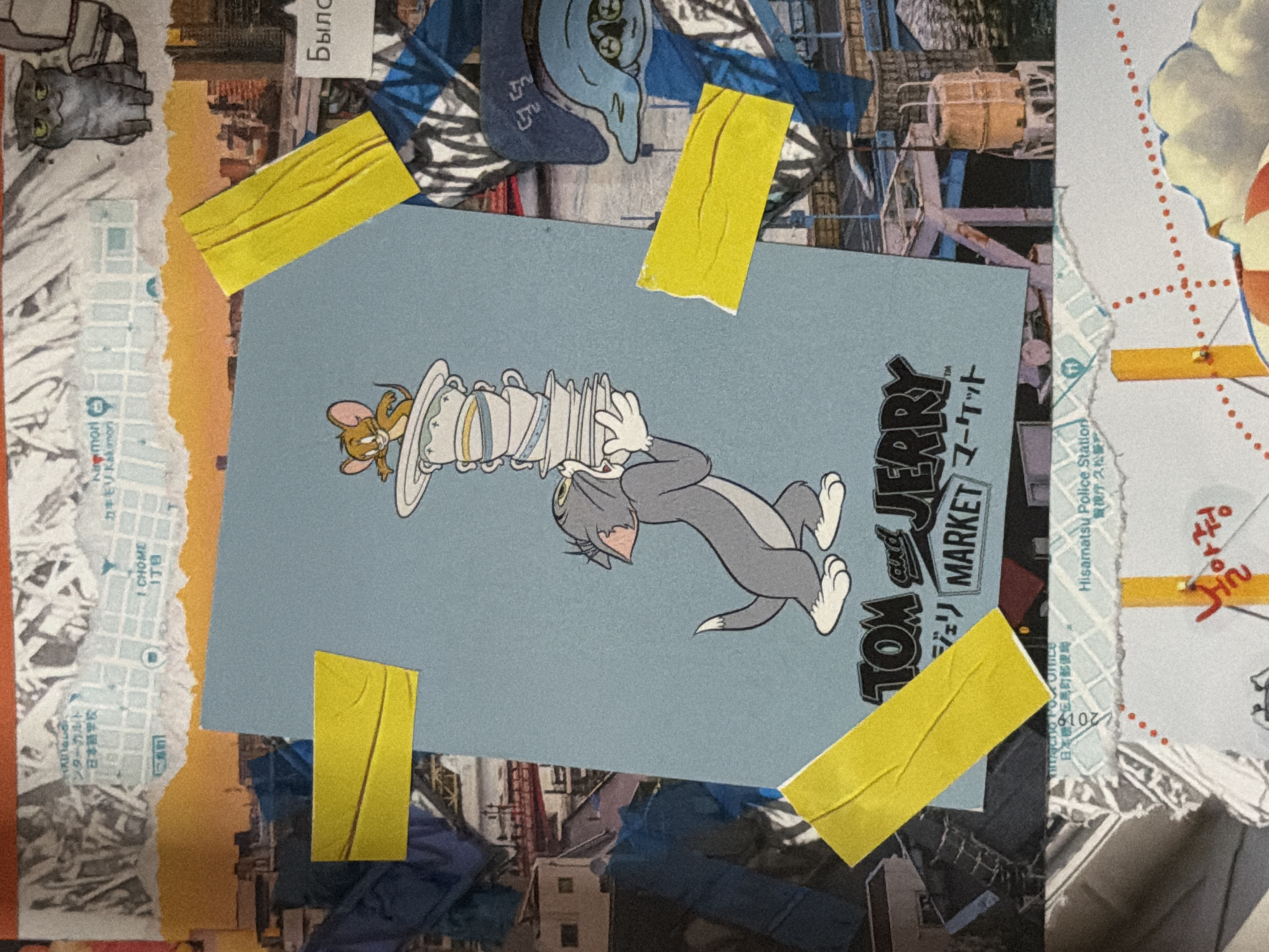 The image is a collage of torn paper scraps featuring a cartoon of Tom and Jerry, a drawing of a cat, and what appears to be fragments of maps and text. One map fragment includes Japanese text, such as "日本学校" (Nihon Gakko - Japanese School) and "I CHOME 17B". Another fragment has Russian text that reads "Было" (Bylo - was/has been). There are also pieces of yellow tape holding some of the fragments together. The collage is layered over a background that includes images of cityscapes and industrial structures. There are no discernible people or specific identifiable locations within the city of Moscow, Russia.