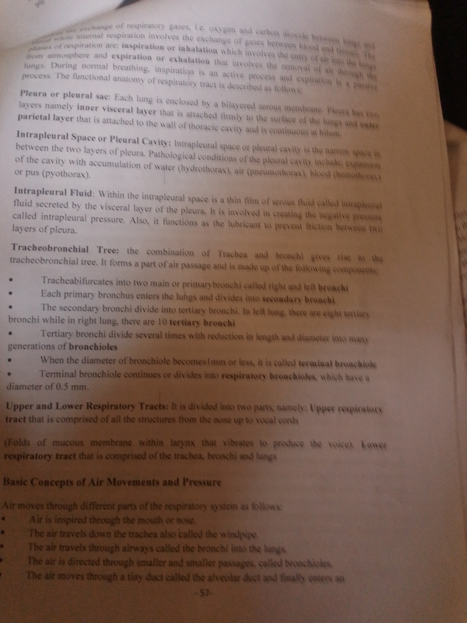 The image shows a close-up of a book with text related to the respiratory system. The page is densely filled with printed words, organized into paragraphs and bullet points, defining terms and explaining processes related to respiration, such as pleura, intrapleural space, and the tracheobronchial tree. Some sections are highlighted with bold text. The text discusses inspiration and expiration, the structure of the lungs, and the path of air through the respiratory tract. There is a page number "-57-" visible at the bottom right of the page. The lighting suggests an indoor environment, likely a study or library, with the focus solely on the open book. No people, objects other than the book, or any environmental cues are visible.