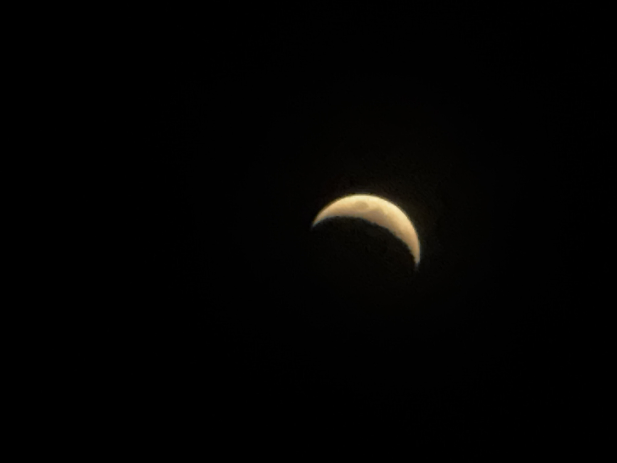 A crescent moon is visible against a completely black background. The moon is situated in the upper-right portion of the frame, with the majority of the image occupied by the blackness of the night sky. No specific landmarks are discernible, preventing identification of Kazan, Russia as the location.