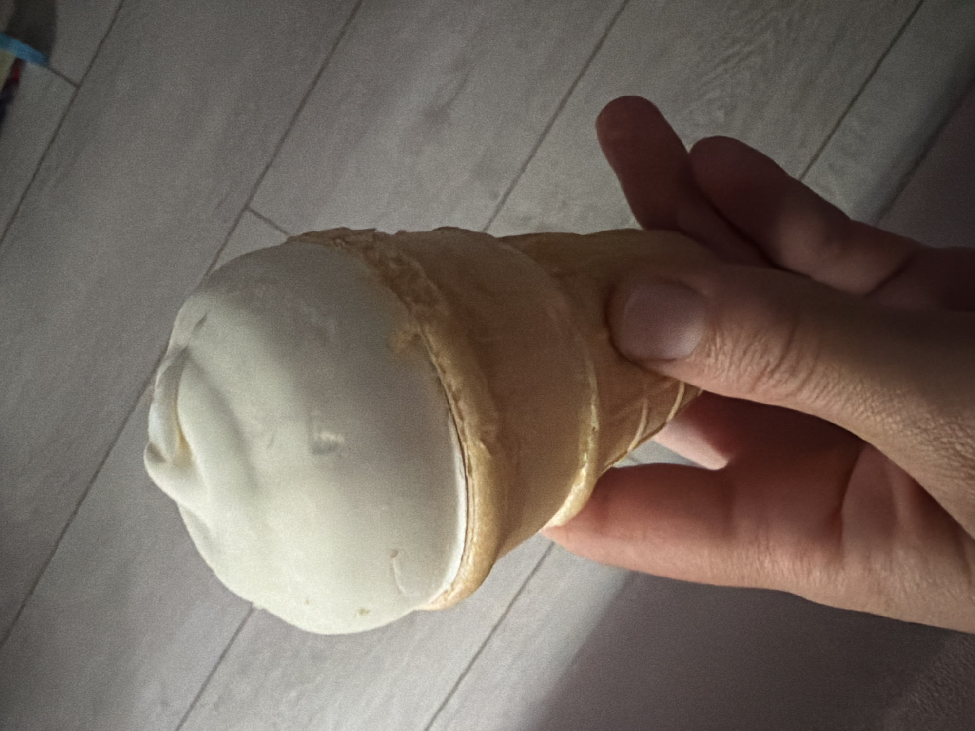 A hand is holding a cream-filled cone. The cone is cylindrical and filled with white cream. The background appears to be a wooden surface. The location and city of Tokkari, Russia are not discernible from the image.