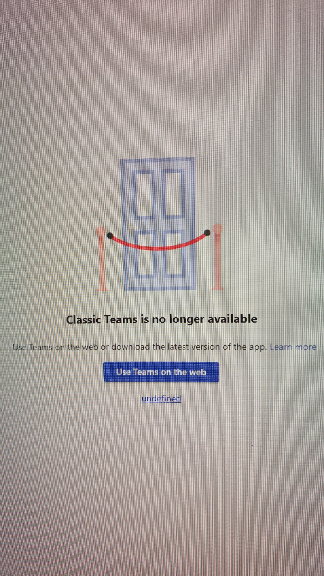 The image shows a screenshot of a computer screen displaying a message that "Classic Teams is no longer available." A stylized graphic of a closed door with red rope barriers in front of it is visible at the top of the screen. Below the graphic, the message is displayed in text, with a button that says "Use Teams on the web." There is also a link that says "undefined". The background of the screen has a faint grid pattern. The image does not contain any information about the city of Kuznetsk, Russia, or any people, subjects, objects, or actions outside of what is displayed on the computer screen.