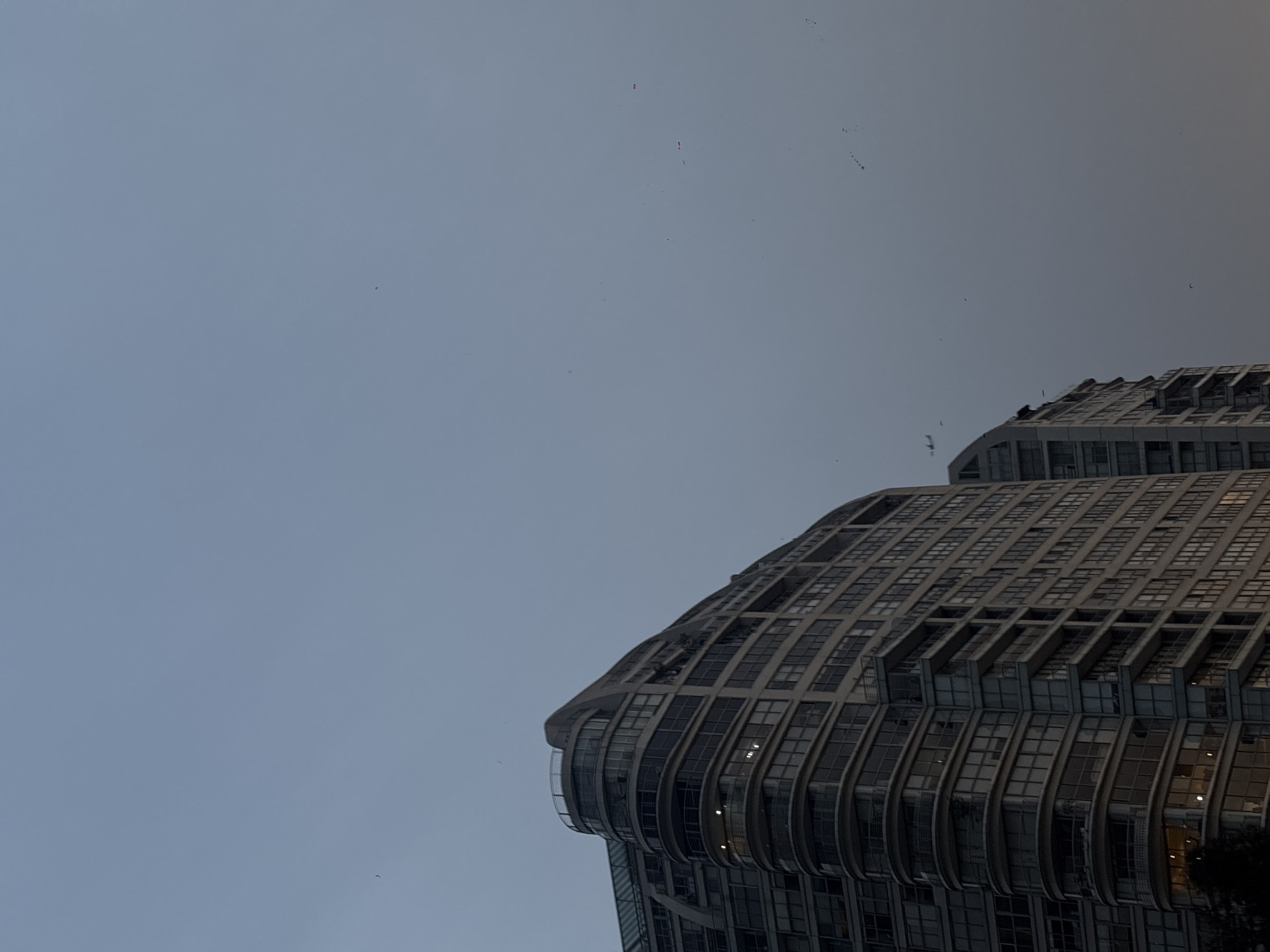 The image depicts a low-angle view of a building against a gray sky. The building is modern, with a curved facade and numerous windows. The image was taken in Mexico City, Mexico.