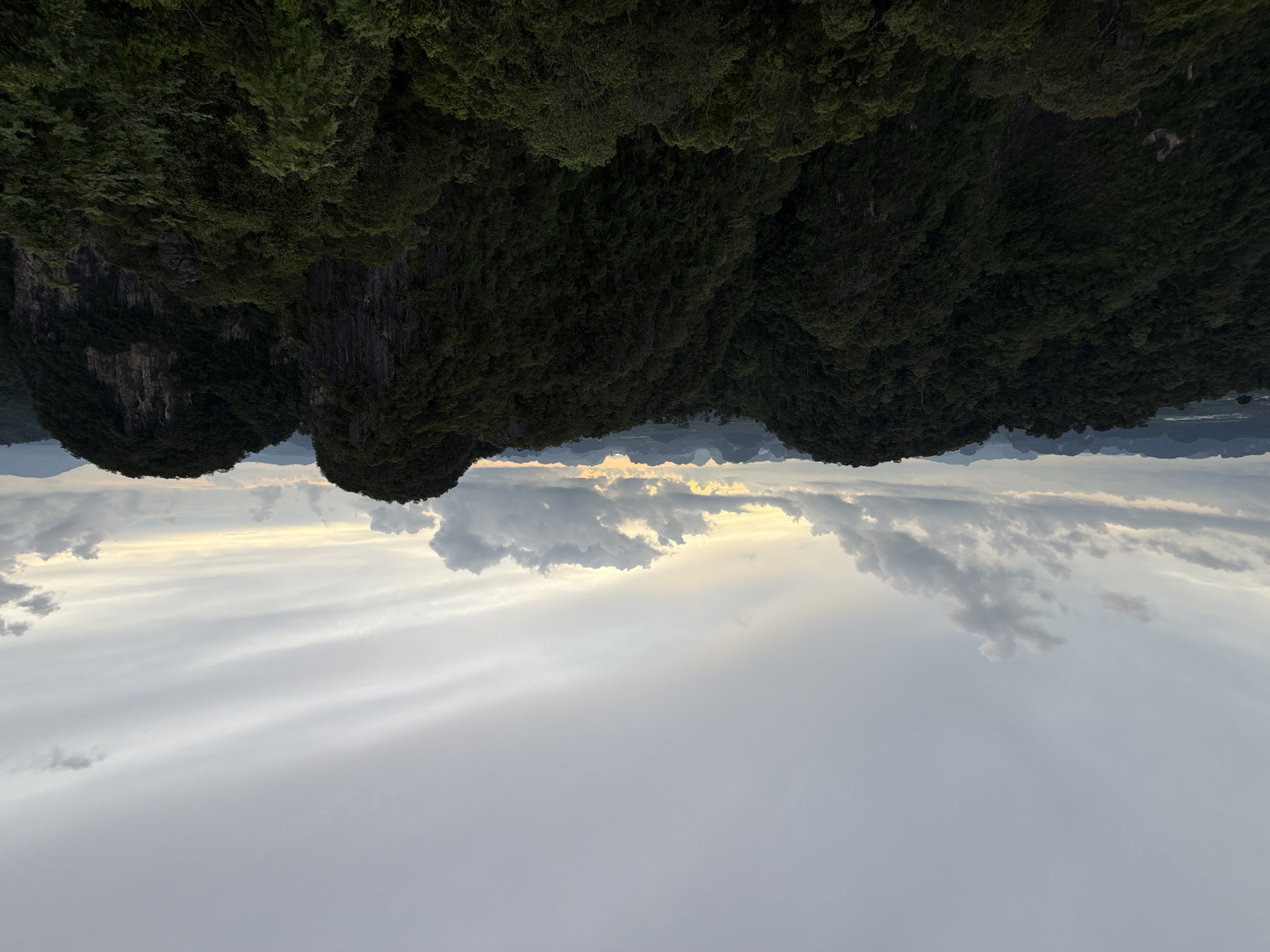 A panoramic, high-angle, outdoor shot captures a dense, dark green forest covering rolling hills and jagged, rocky outcrops under a cloudy, overcast sky. The horizon is lined with distant, hazy mountain ranges. The lighting suggests either early morning or late afternoon. The scene is devoid of any people or structures. The location is identified as being in Ban Khao Tang, Thailand.