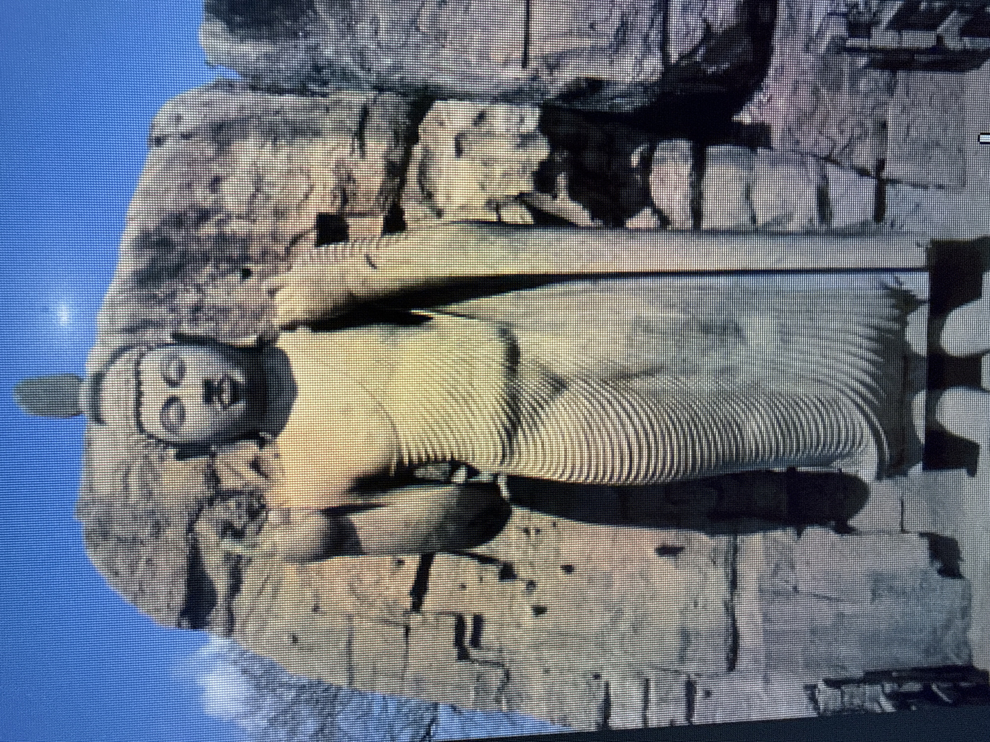 Here is a detailed description of the image:
The image shows a large reclining Buddha statue carved into a cliff face or rock formation. The statue is weathered and appears to be made of stone. The Buddha is lying on its right side, with the head resting on the right hand. The facial features are visible, including eyes, nose, and mouth. The robe appears to be draped over the body. The statue is set against a background of rocky terrain and a blue sky.
Given the style and subject, this could be a depiction of a Buddhist monument. However, I cannot confirm the location in Sofia, Bulgaria, as the visual evidence does not provide any specific clues or context that links the image to that location.