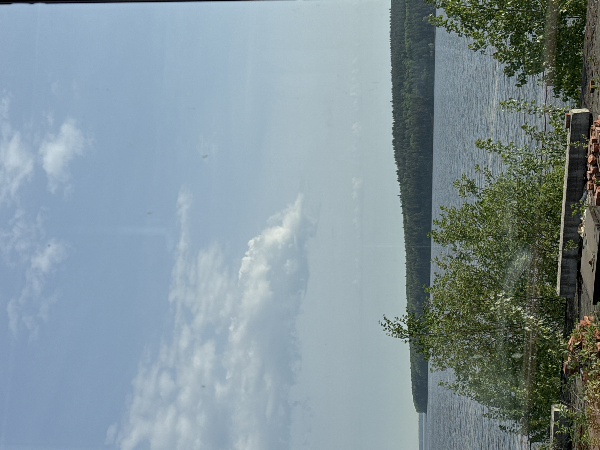 The image shows a landscape with a lake, forest, and sky with clouds. A small section of a building or structure is visible on the right side, potentially indicating an urban setting nearby. Without further context, pinpointing the exact location in Chaikovsky, Russia, is difficult, as such features could be found in multiple areas around the city.