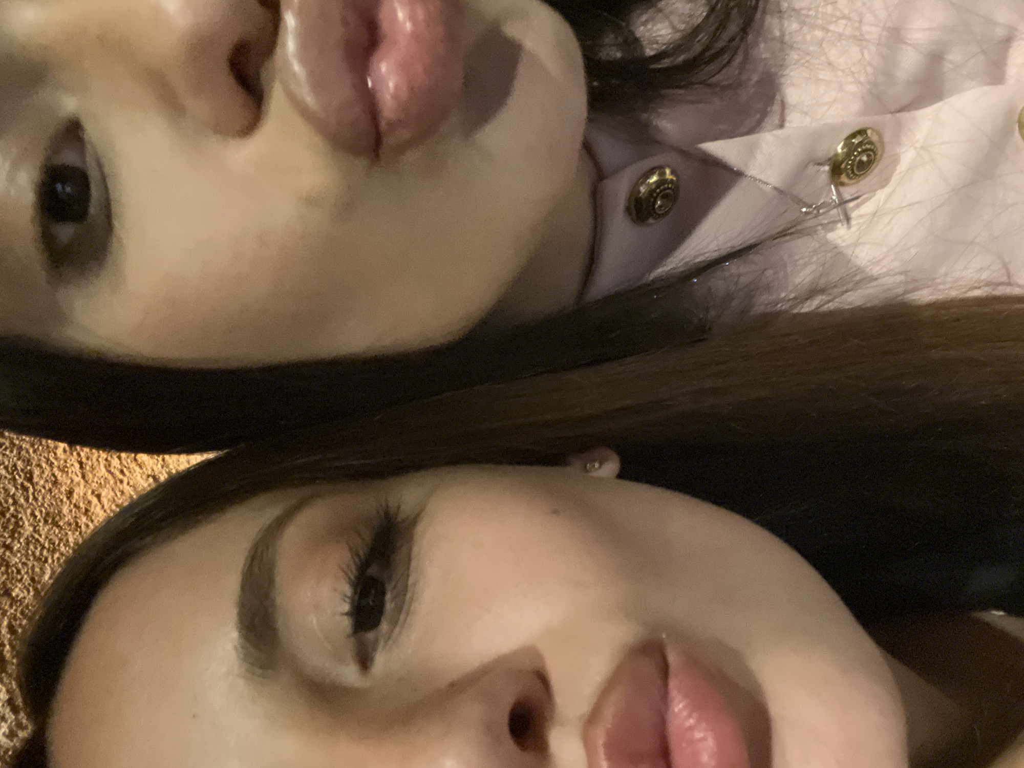 Two women are lying next to each other, close-up view of their faces. The woman on top has dark hair and is wearing a light pink top with gold buttons. The woman below has brown hair. The location is Yerevan, Armenia, is unknown.