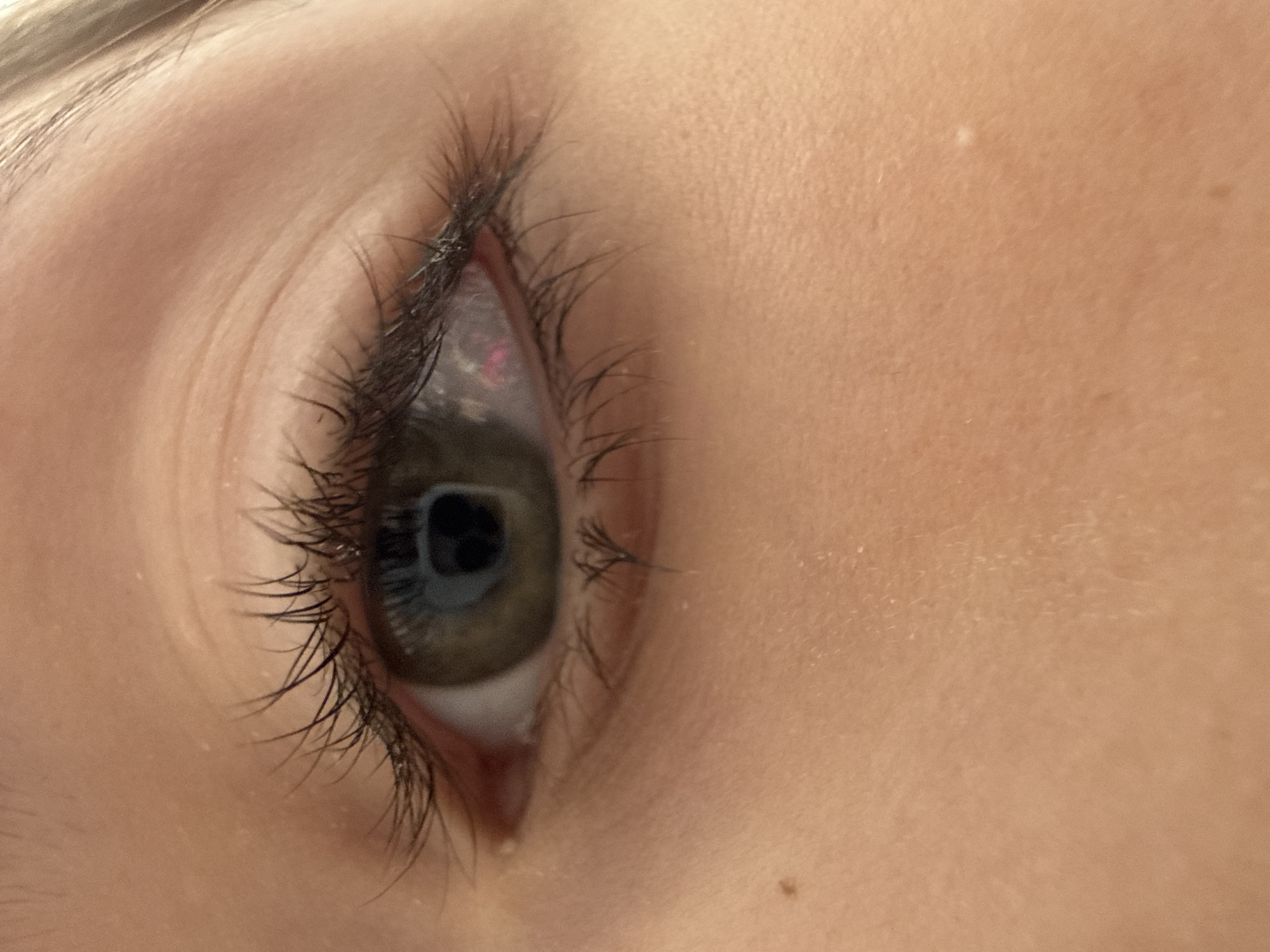 A close-up view of a human eye, angled from the side. The eye has dark lashes, and the iris appears to be a mixture of green and brown hues. The surrounding skin has a light, warm tone. There are no discernible elements to place the image within a specific location, such as the city of Votkinsk, Russia.