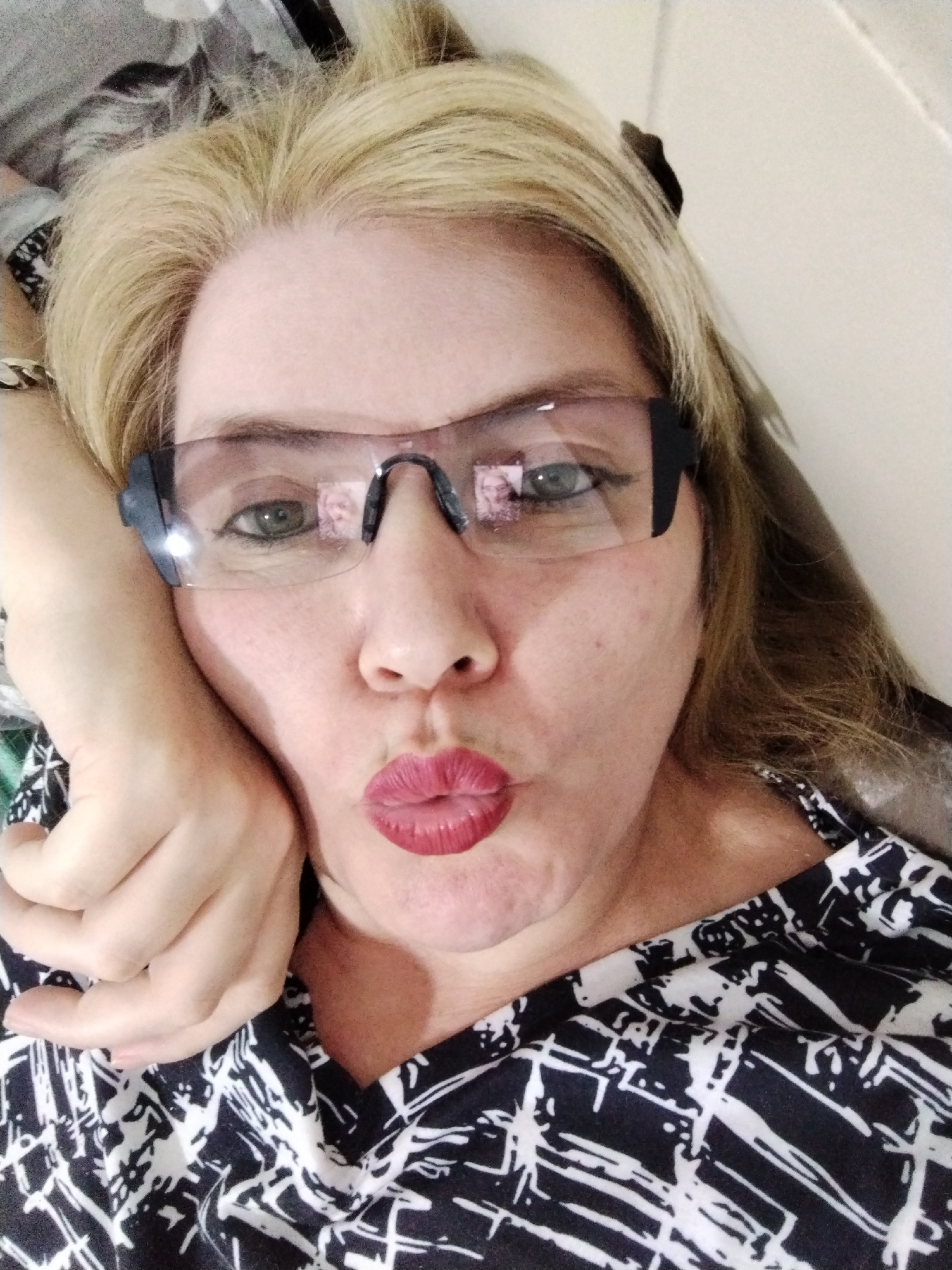 A woman is lying down, wearing safety glasses and red lipstick, with her hand near her face. She has blonde hair and is wearing a black and white patterned shirt. The location of the photo is unknown, and there is no indication of Al Mas'oudi or the United Arab Emirates.