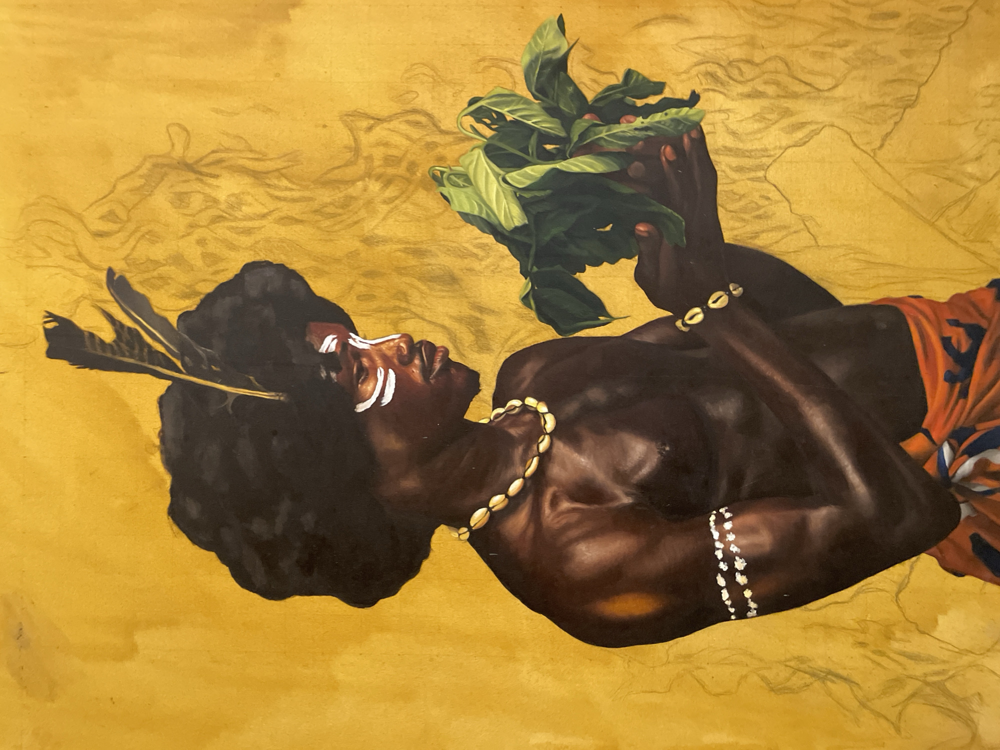 A portrait depicting an African man, adorned with white face paint, feathers in his hair, a shell necklace, and a beaded bracelet, is shown holding a cluster of green leaves with red berries. He is clad in a patterned orange garment. The background is a textured yellow with faint drawings. The location is identified as Ado, Nigeria.