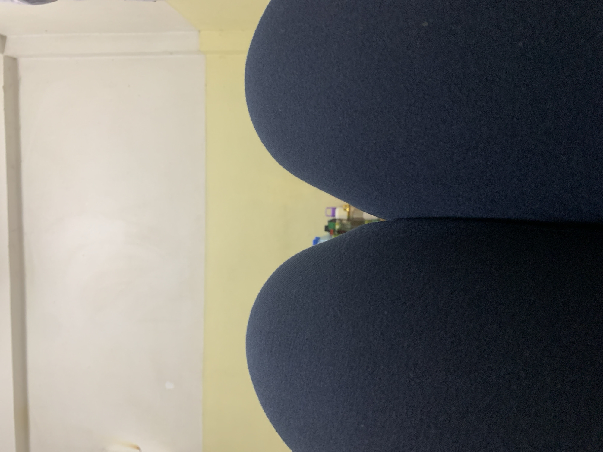 The image shows a close-up of two navy blue, curved objects, possibly cushions or parts of a chair. They are positioned against a background of two walls. One wall is off-white, while the adjacent wall is a pale yellow. The location cannot be determined from the image. No people or actions are visible.