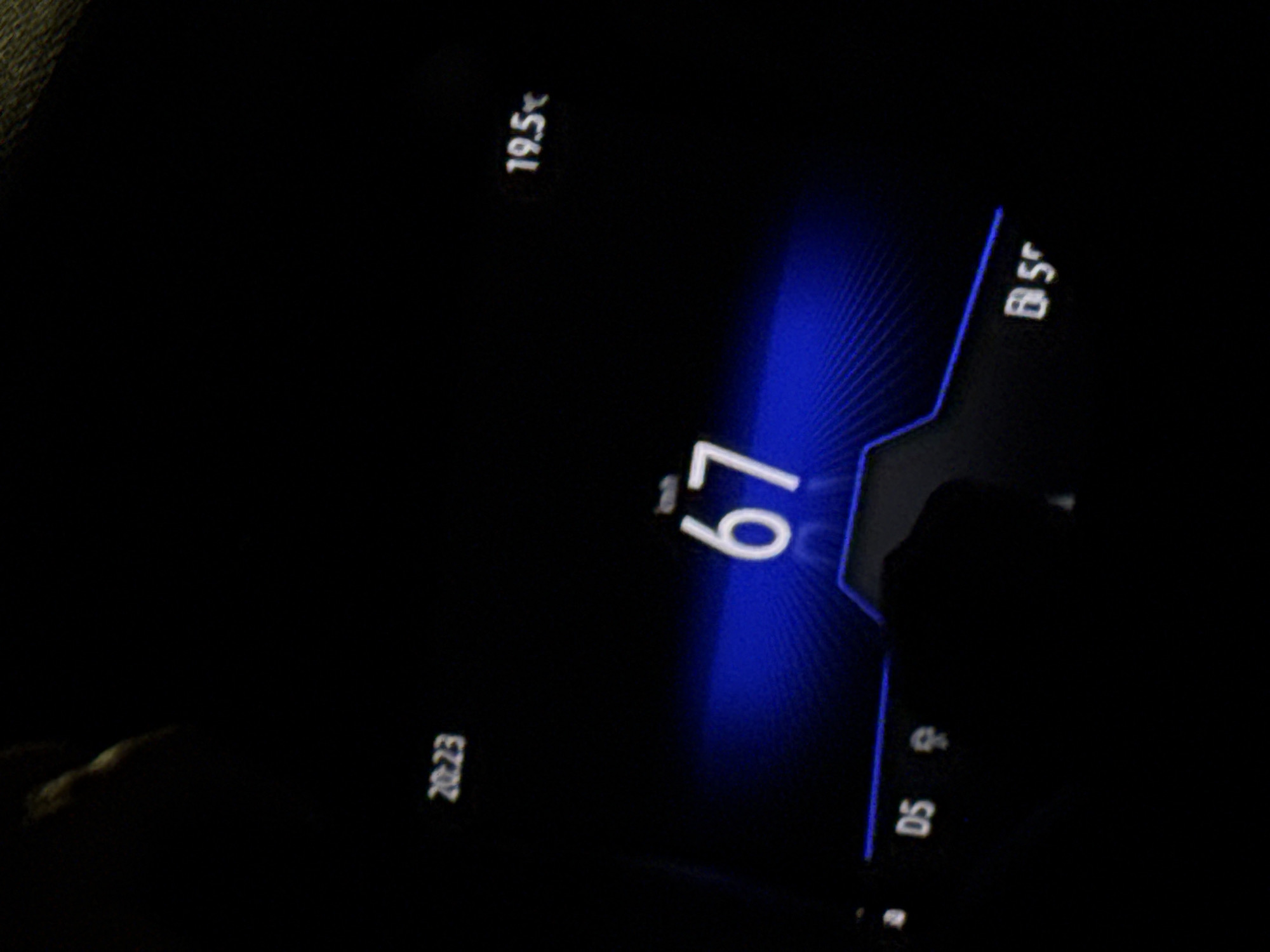The image shows a digital display, likely from a car's dashboard, indicating a speed of 67, a temperature of 19.5, a time of 20:23, and "DS" along with an icon, and "BS" with an icon. The environment is dark. The location is unknown.