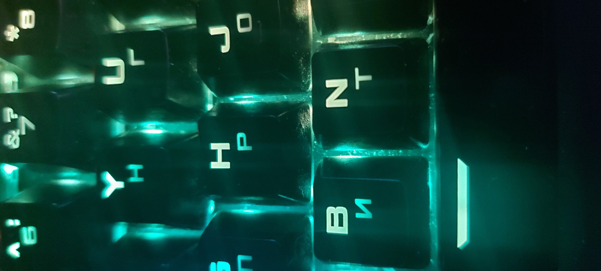 The image shows a close-up view of a backlit keyboard, likely a mechanical keyboard with customizable RGB lighting. The keycaps are black with white legends. The camera angle is slightly skewed. The keys visible show symbols that appear to be a mix of Latin and Cyrillic characters, or possibly mathematical notations. Individual keycap legends visible include "N+", "Hp", "BИ", "I", "JL", and "JO". The scene appears to be indoors with low ambient lighting, as the backlighting of the keyboard is the dominant light source.
There is no indication in the image of the city of Tashkent, Uzbekistan.