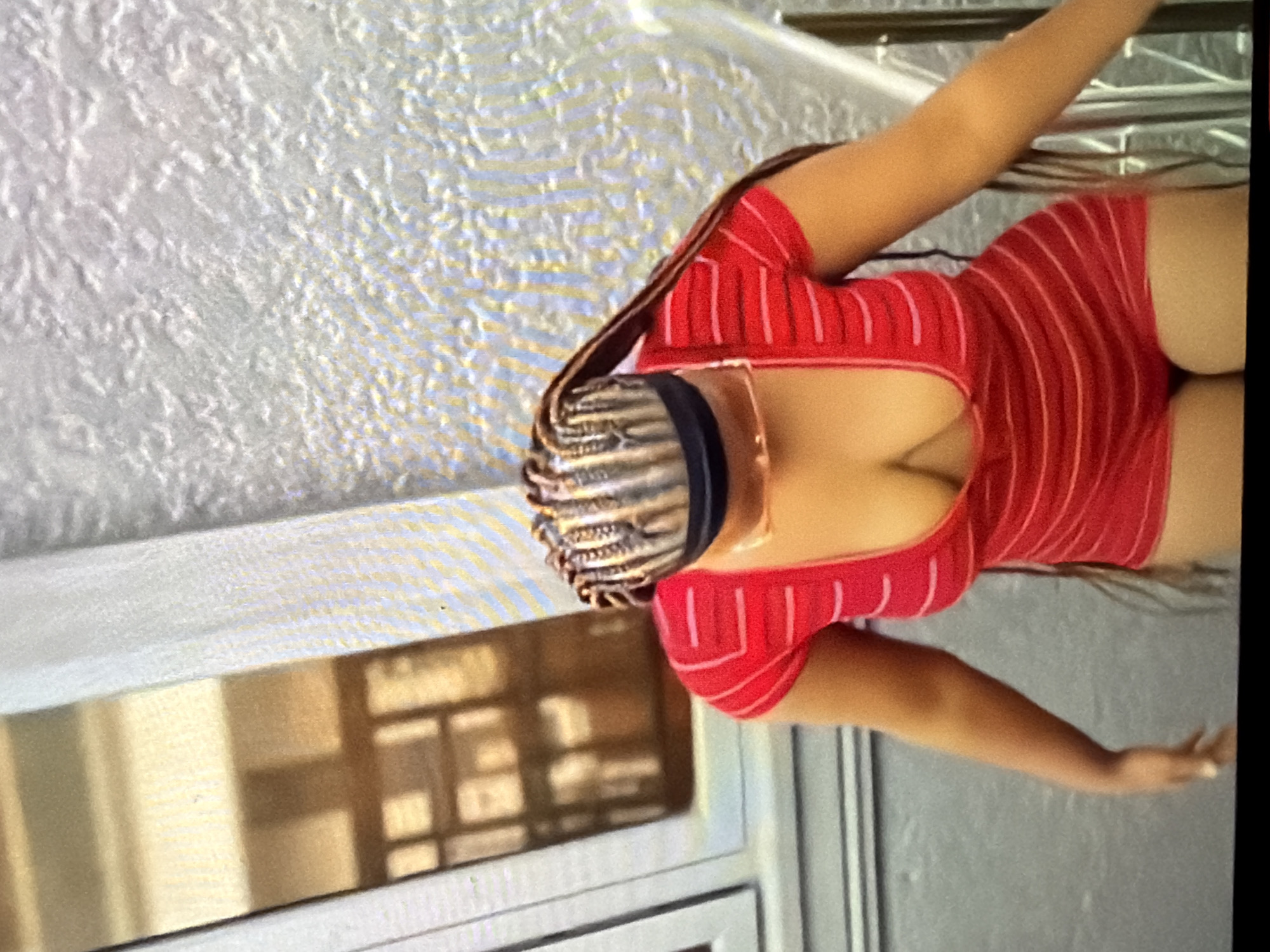 A woman with braided hair and a red and white striped top is walking down stairs. She is wearing sunglasses. The background is a wall with a textured pattern. The location is Bukuru, Nigeria.