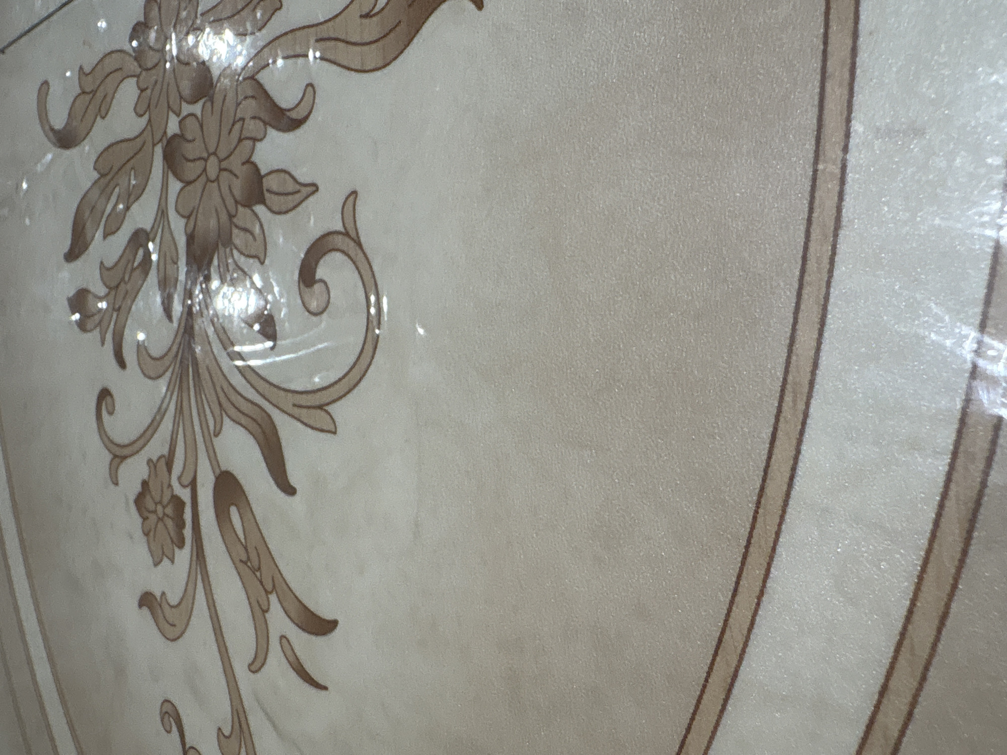 The image shows a close-up of a surface with a floral design and geometric border. The design is in shades of beige and brown. The surface appears to be covered with a protective layer of plastic. While it is not possible to determine the exact location in the city of Chaikovsky, Russia from the image alone. There are no people or actions visible in the picture.