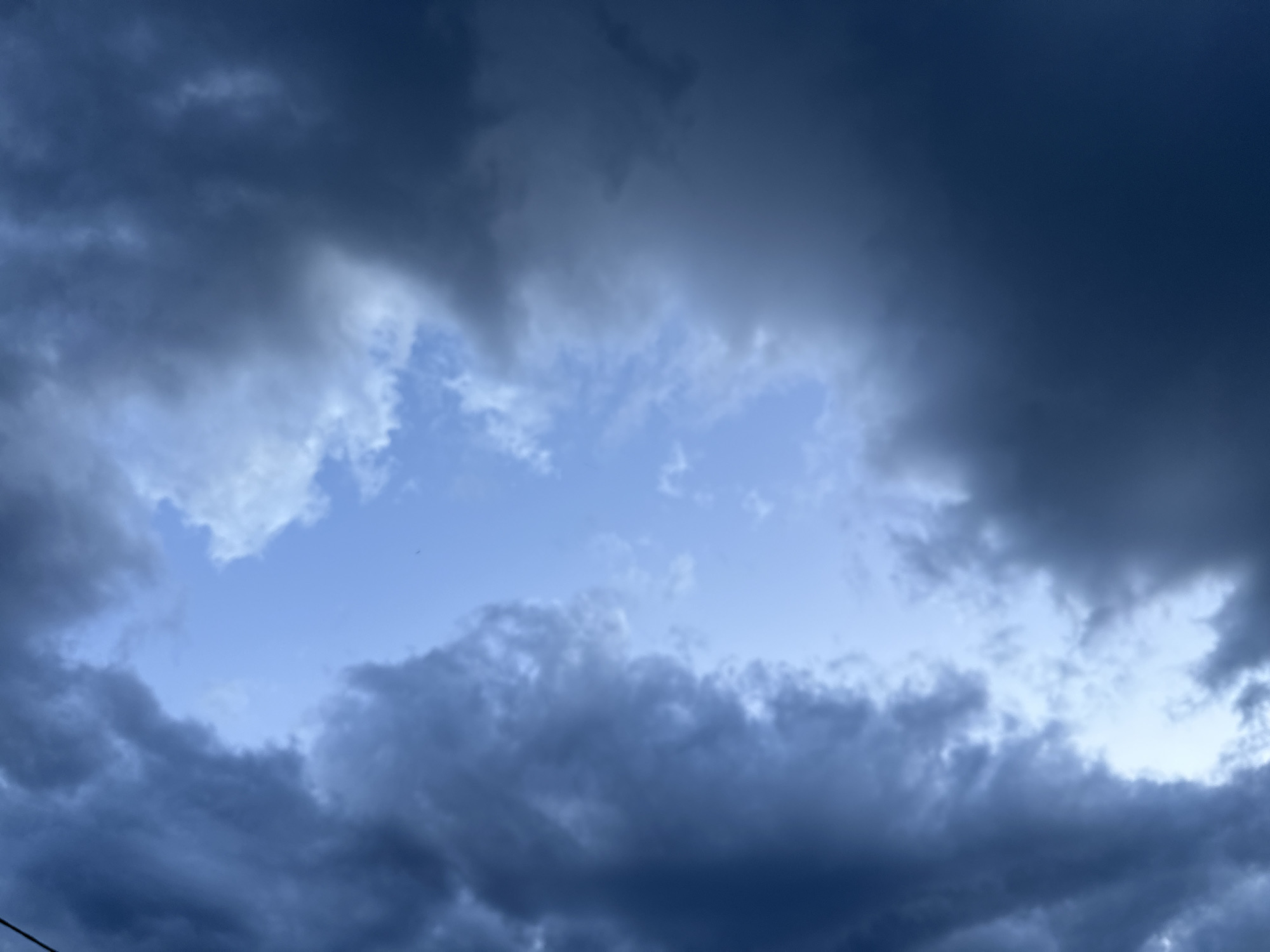 The image shows a sky filled with dark, ominous storm clouds. A small opening in the clouds reveals a patch of lighter blue sky. The scene appears to be an outdoor shot, likely taken from ground level, looking upwards. There are no people, subjects, or specific objects clearly visible, besides the clouds and the sky. The environment is characterized by the atmospheric conditions, suggesting an approaching or ongoing storm. The location is specified as Chepintsi, Bulgaria.